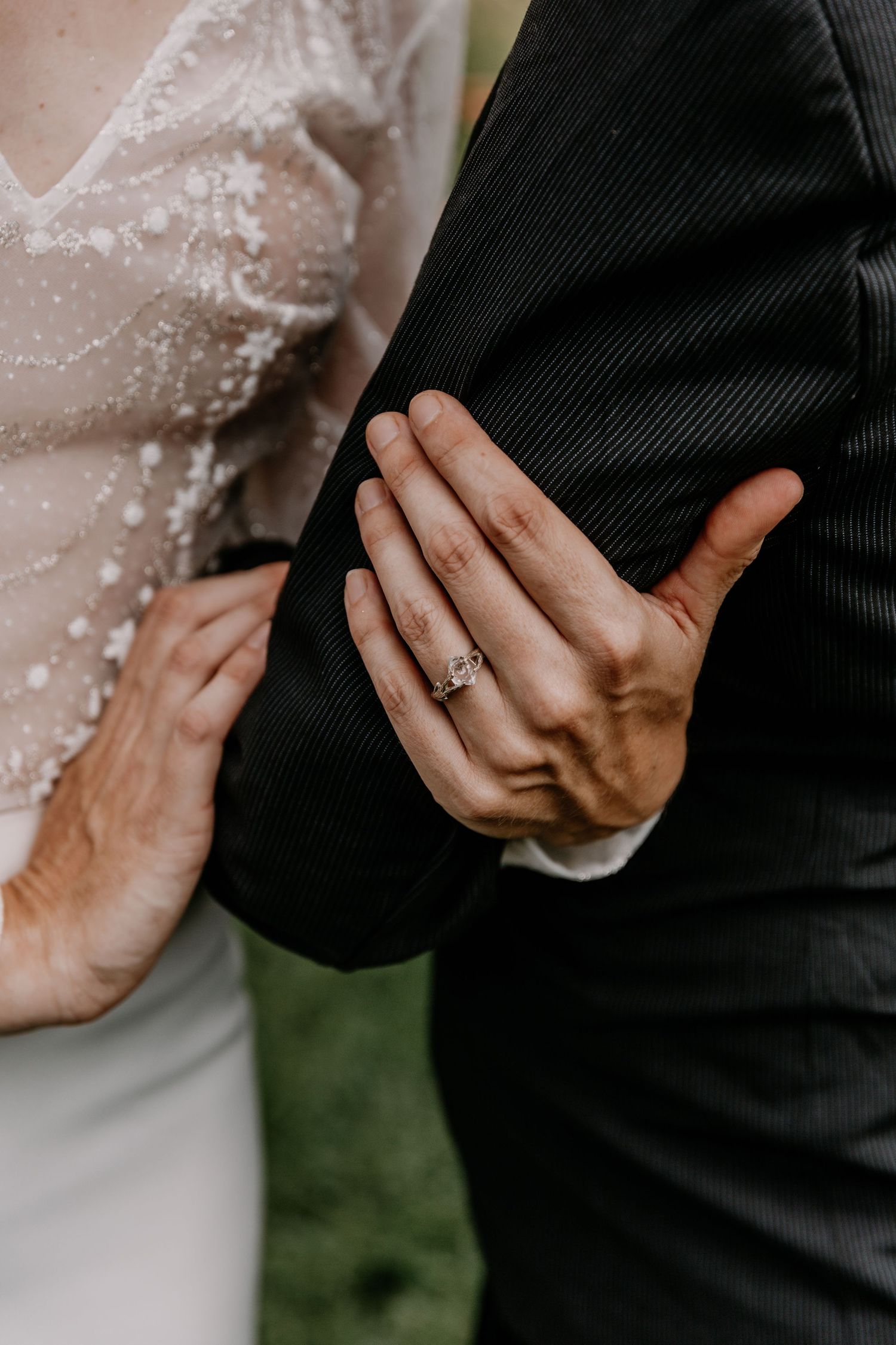 Close-up of hands gently touching during a wedding ceremony, showing delicate lace sleeve details.