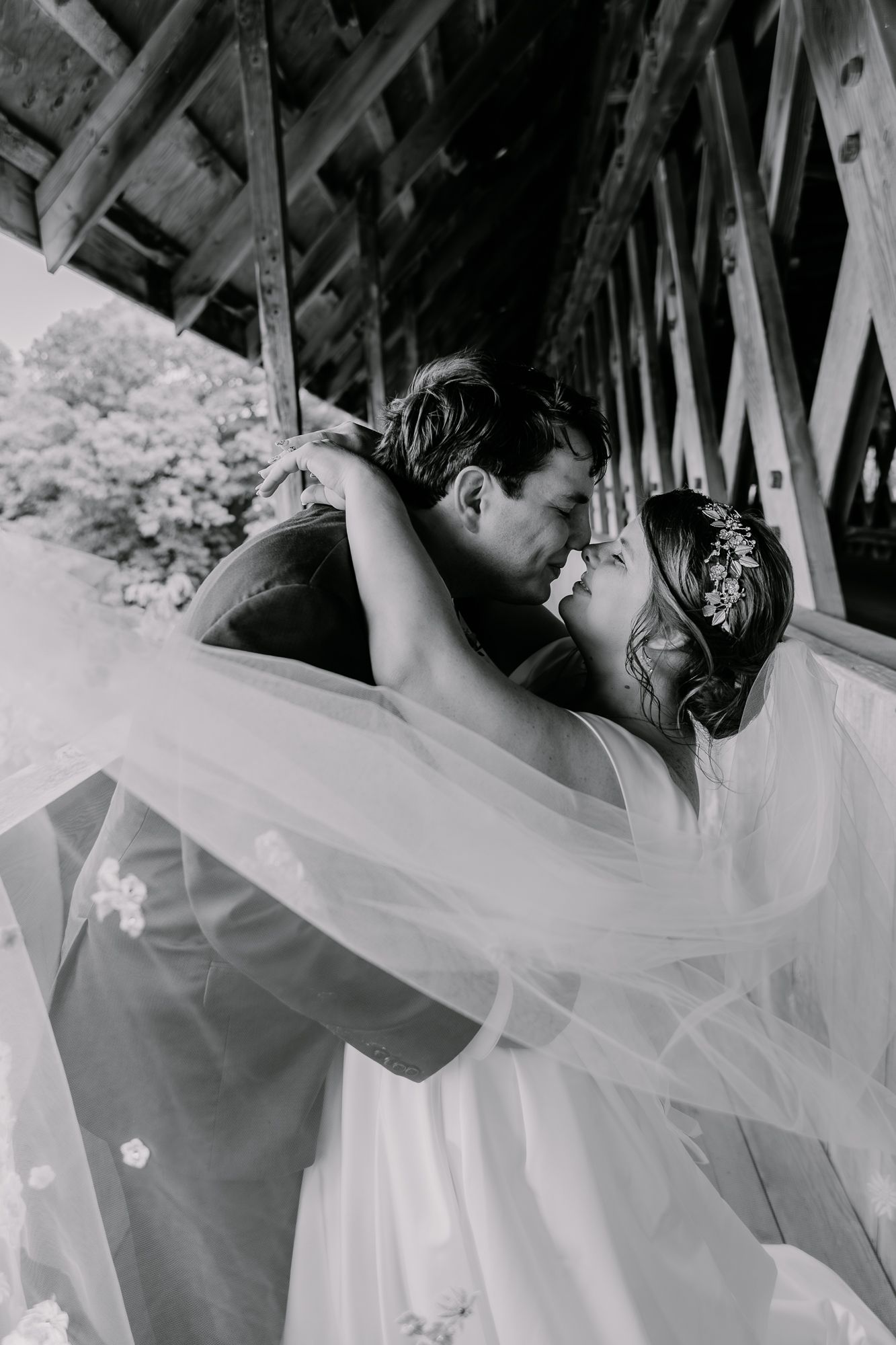 A romantic wedding couple sharing an intimate kiss under a wooden bridge structure.