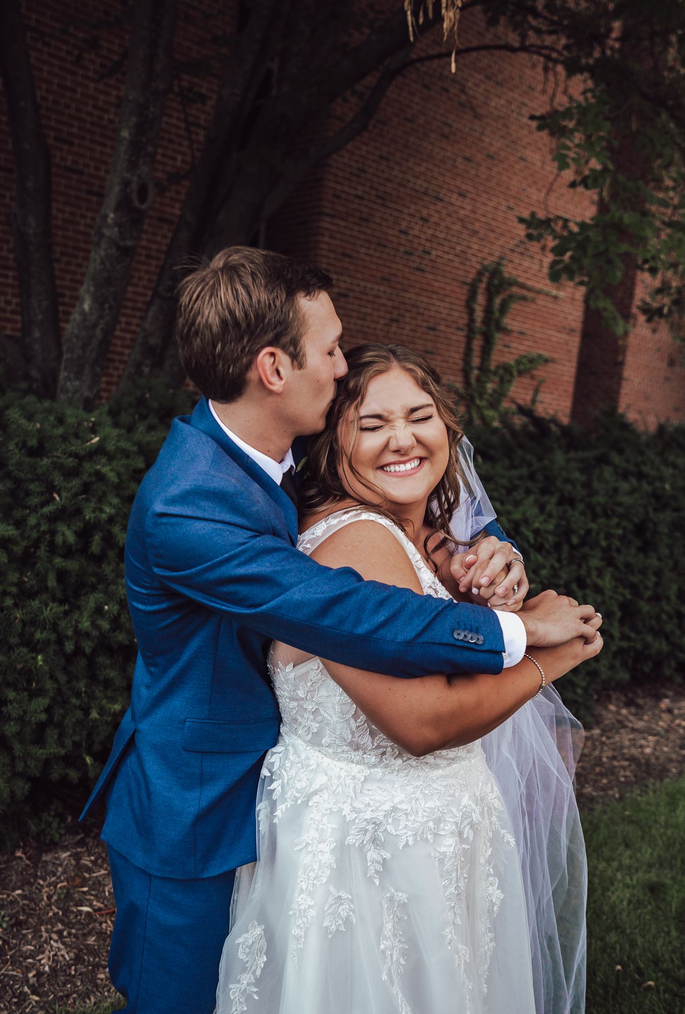 Candid moment of groom embracing bride from behind as they share a laugh.