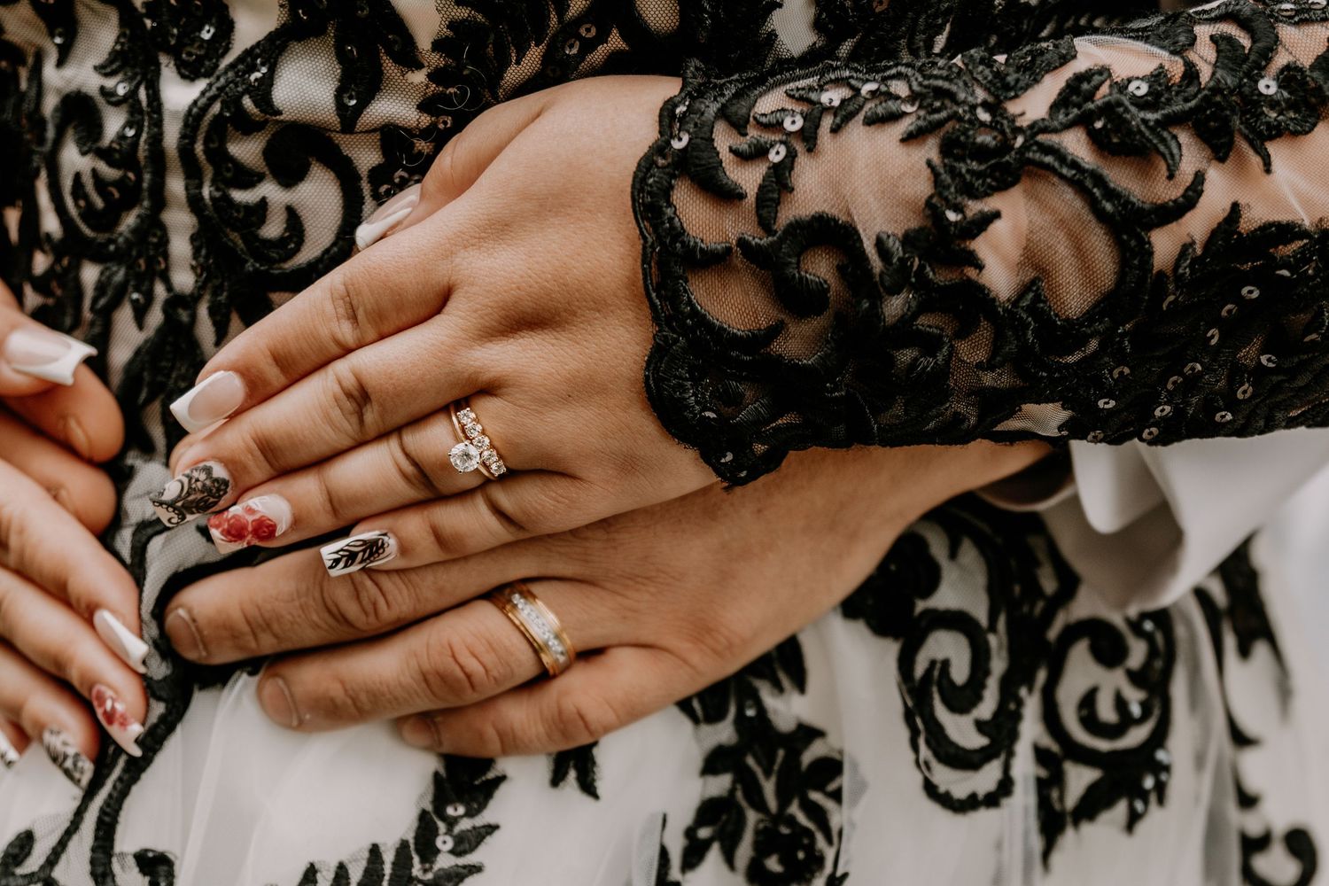Close-up of hands showing wedding rings against black and white lace dress details.