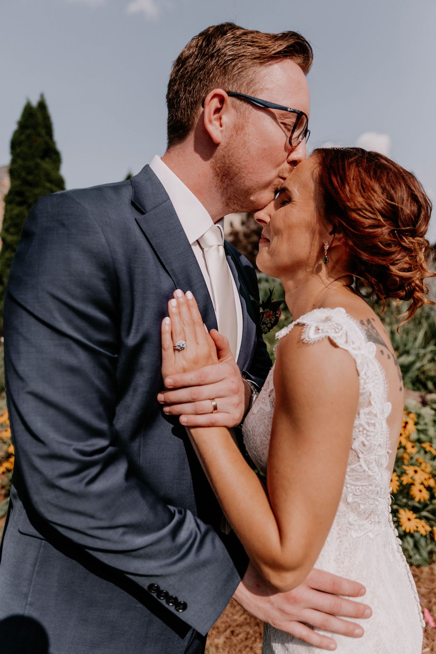 Close-up portrait of newlyweds sharing an intimate moment in front of cypress trees.