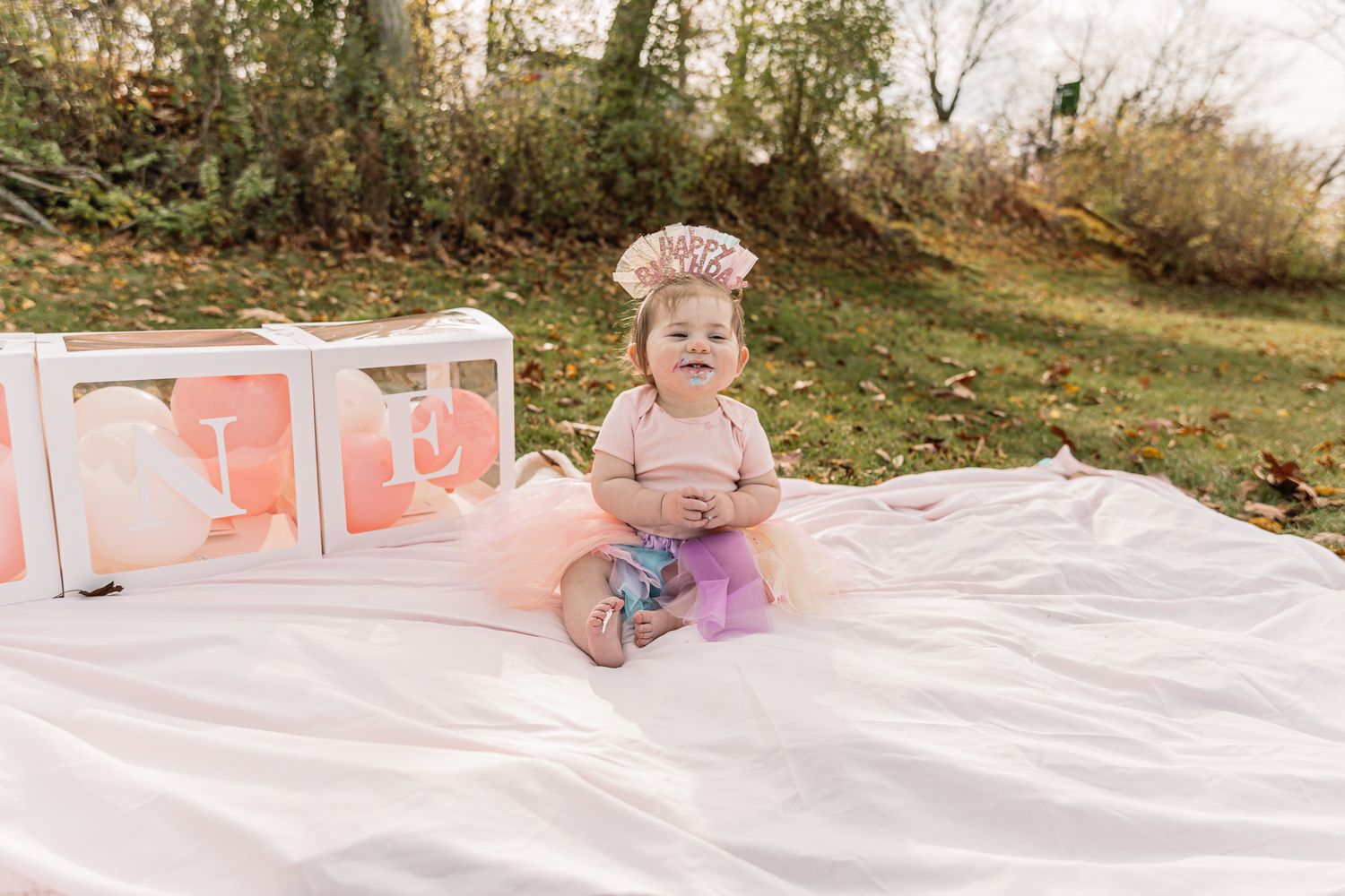 Small child in floral outfit posing with pink letter blocks on white blanket.