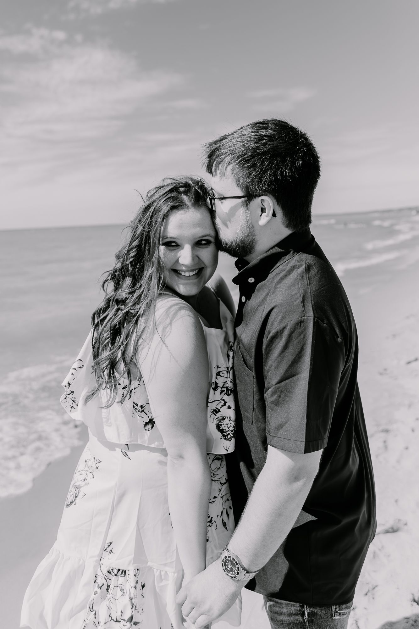 A black and white portrait of a couple sharing an intimate moment on a beach.