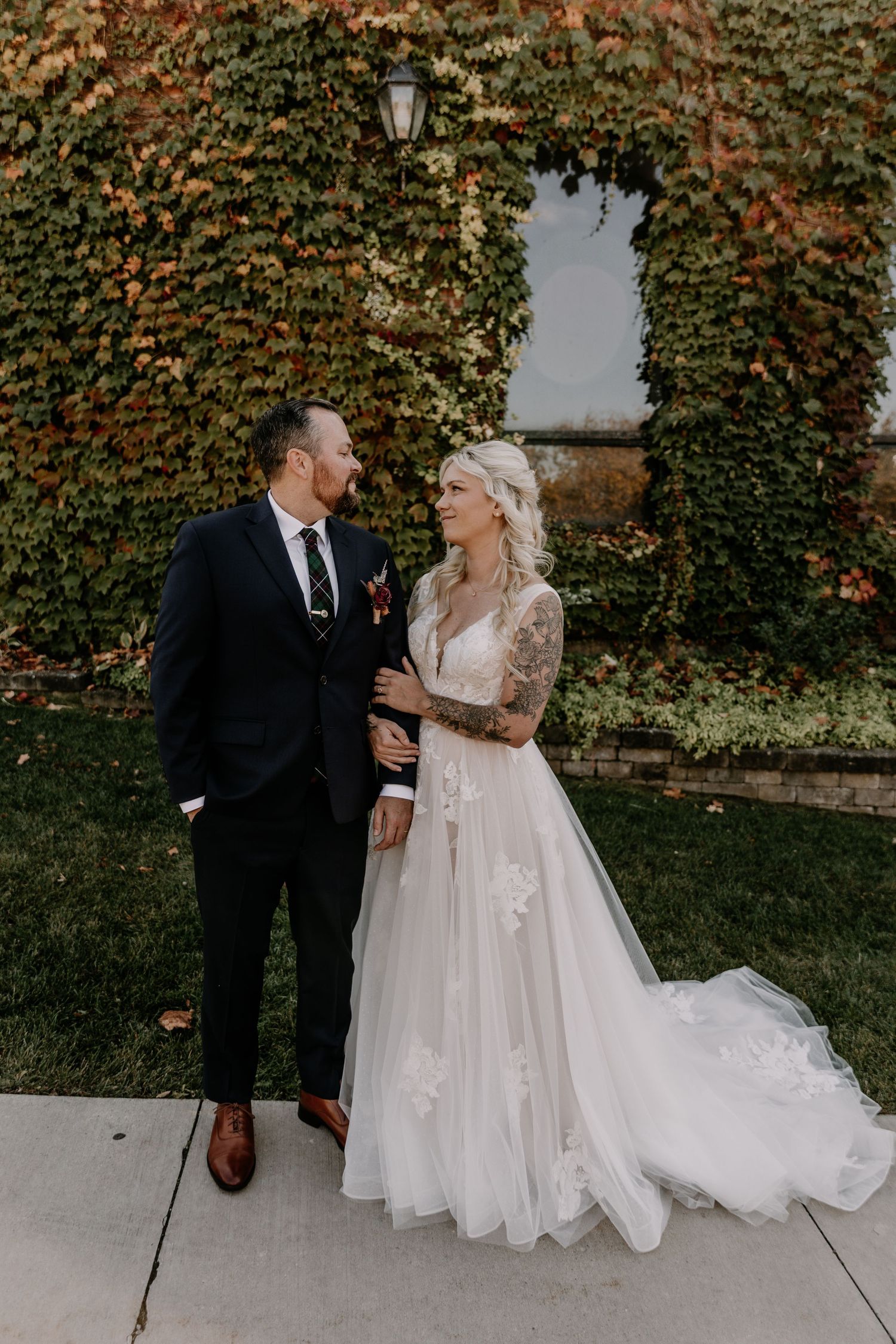 A wedding couple poses in front of an ivy-covered wall with a vintage lantern on an autumn day.