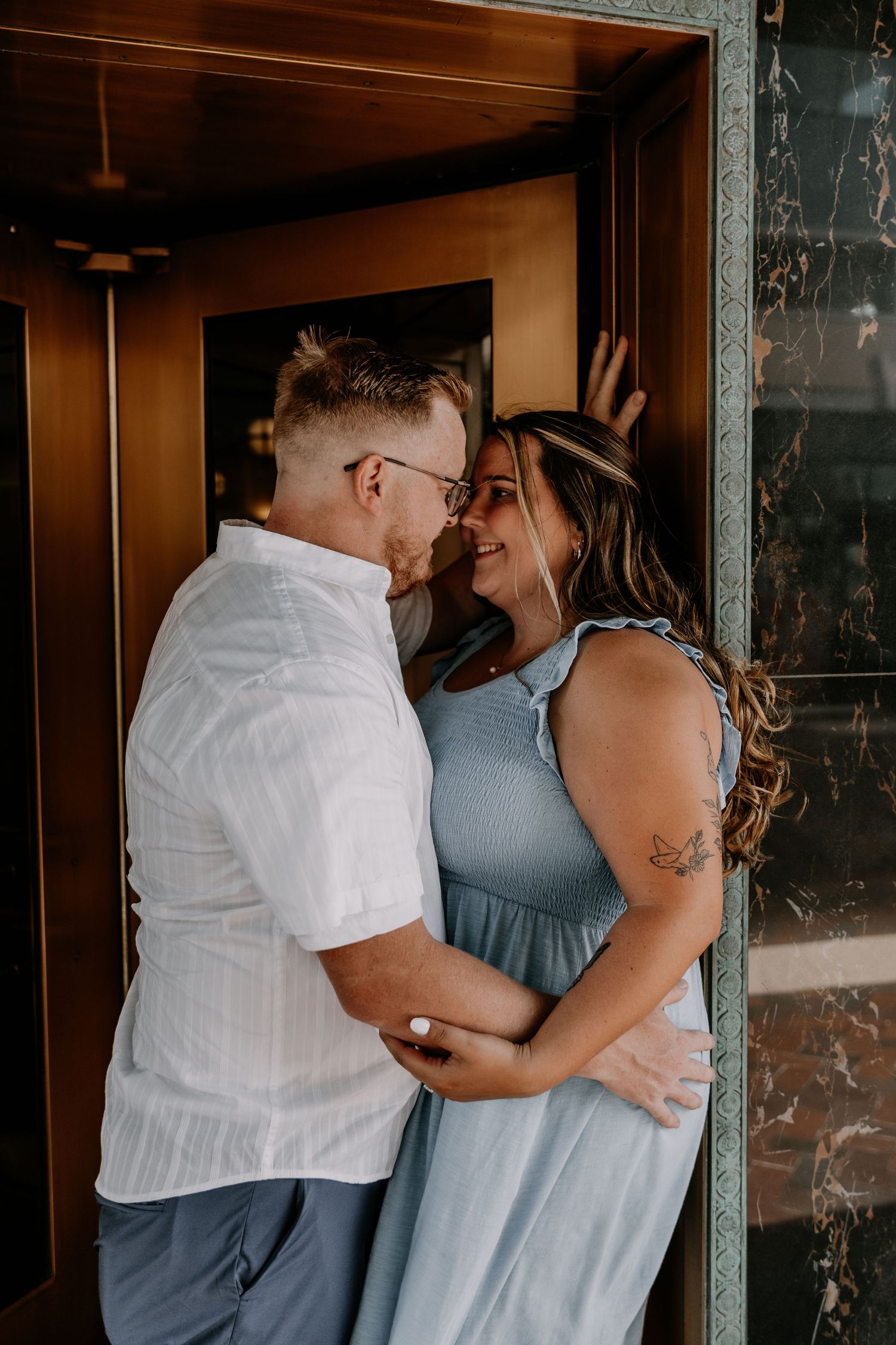 A couple in blue and white outfits share intimate moments in a series of romantic poses against a rustic wall.