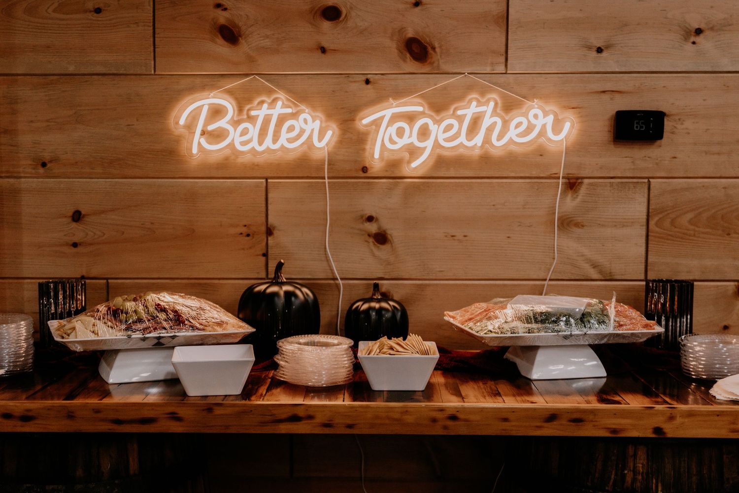 A buffet table with 'Better Together' neon sign on wooden wall displays food and serving dishes.