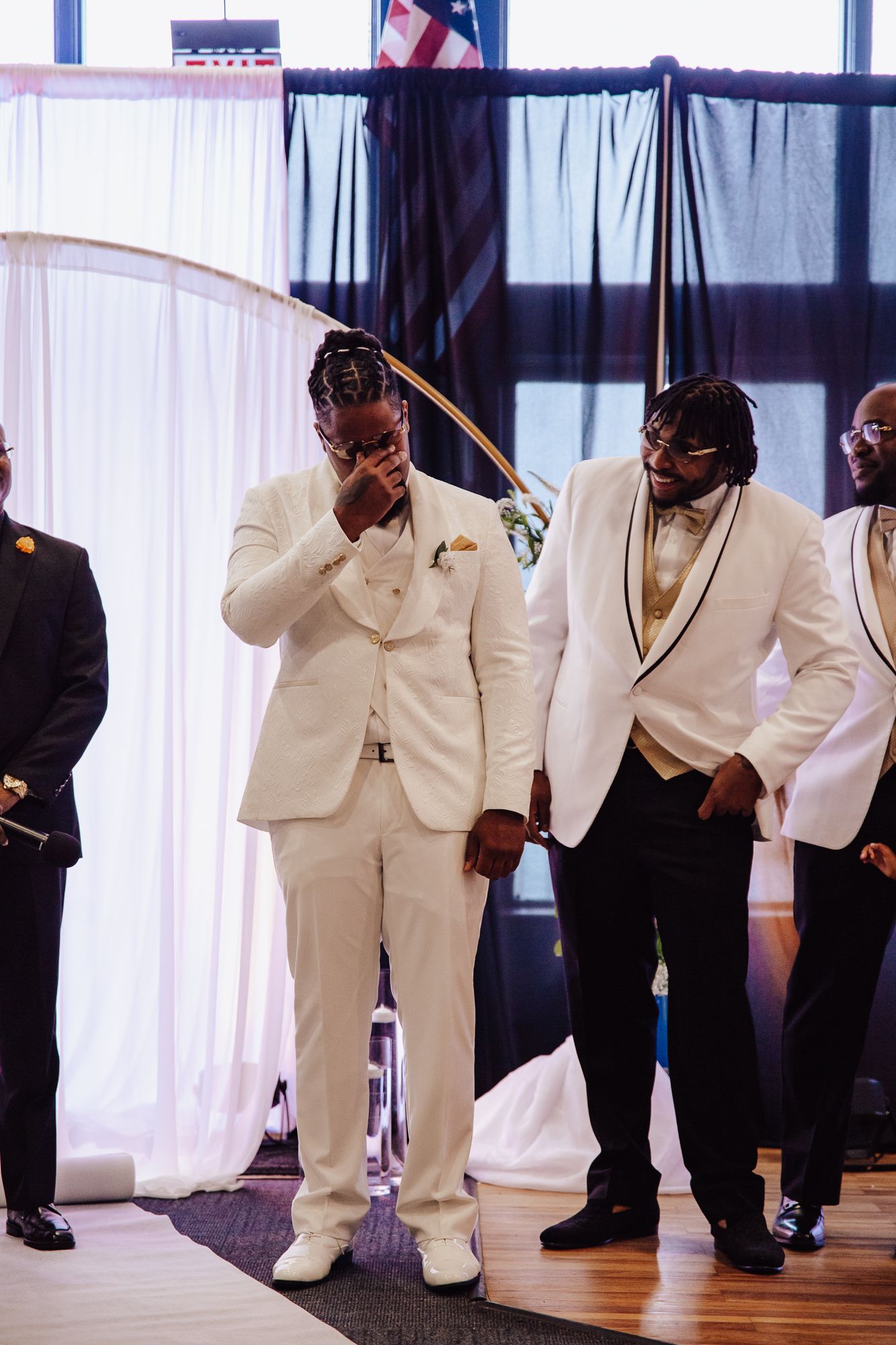 Emotional moment as groom in white suit wipes tears during wedding ceremony.