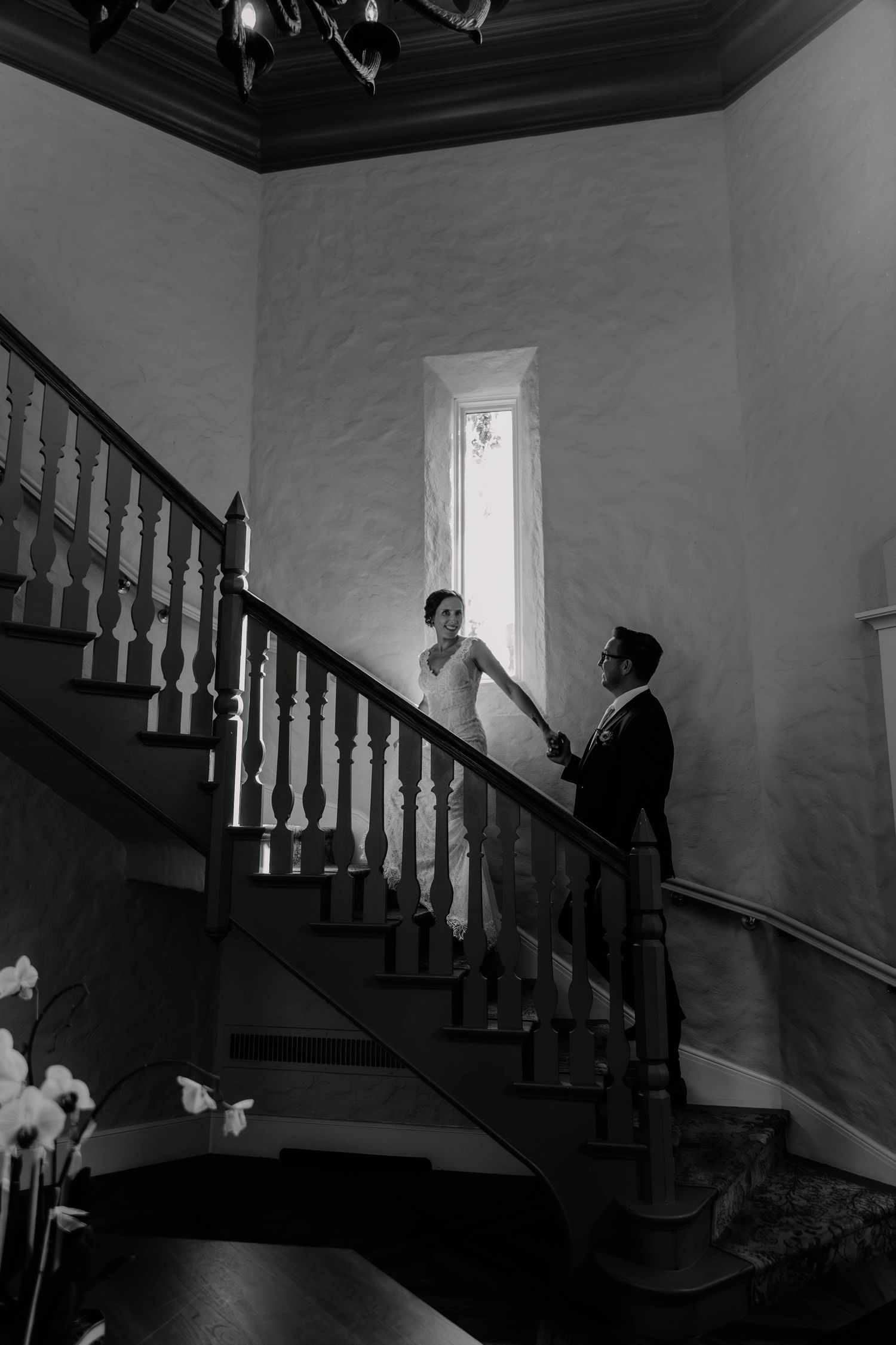 A vintage black and white photo showing a bride and groom on an elegant staircase in a historic building.