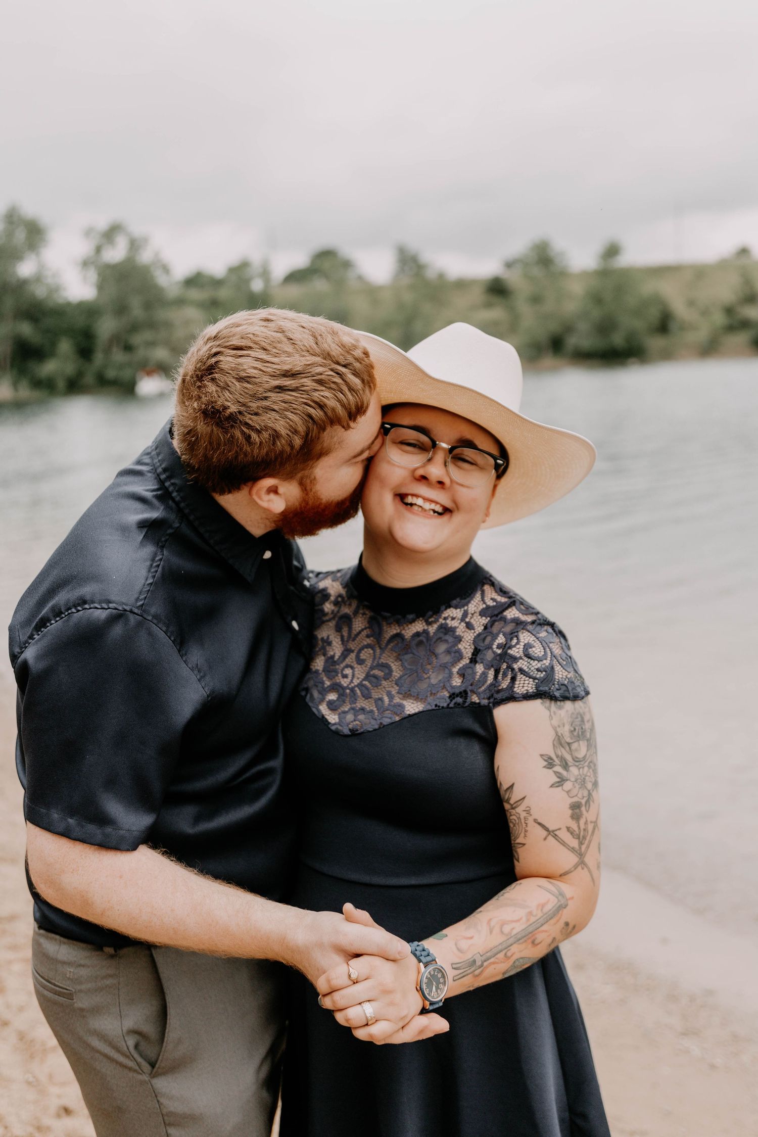 Joyful moment captured between couple on sandy beach with lake in background.