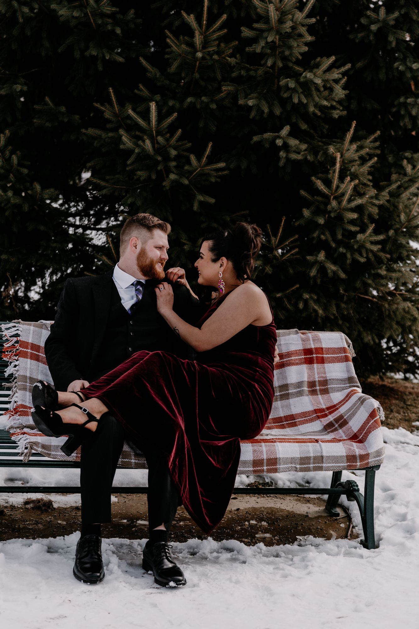 A couple sitting on a plaid blanket in the snow sharing a playful moment.