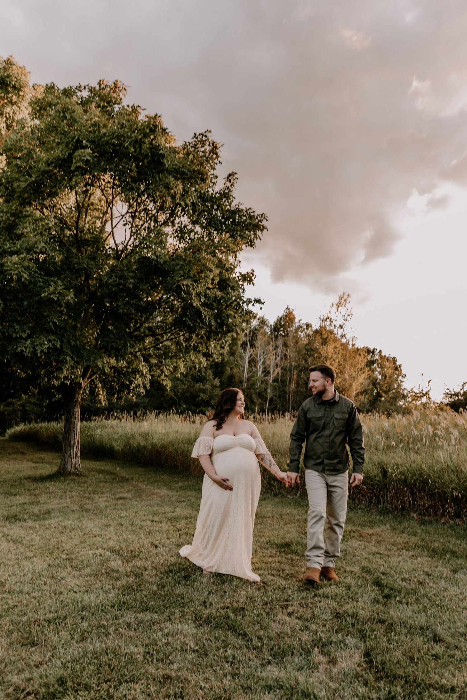Two people enjoy a playful moment together on a grassy hill during golden hour with trees in the background.
