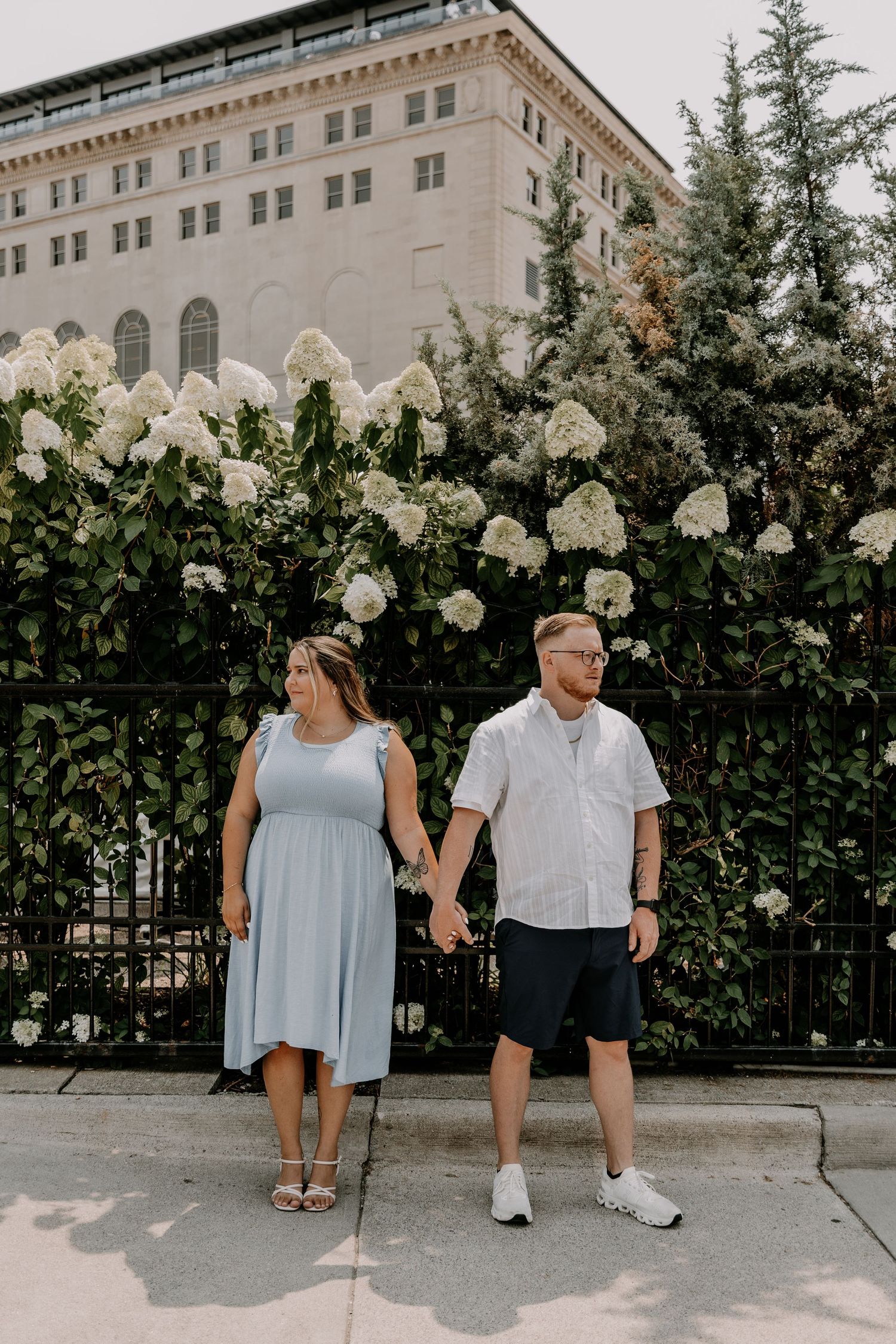 A couple sits on concrete steps bordered by flowering white hydrangeas and a historic building facade.