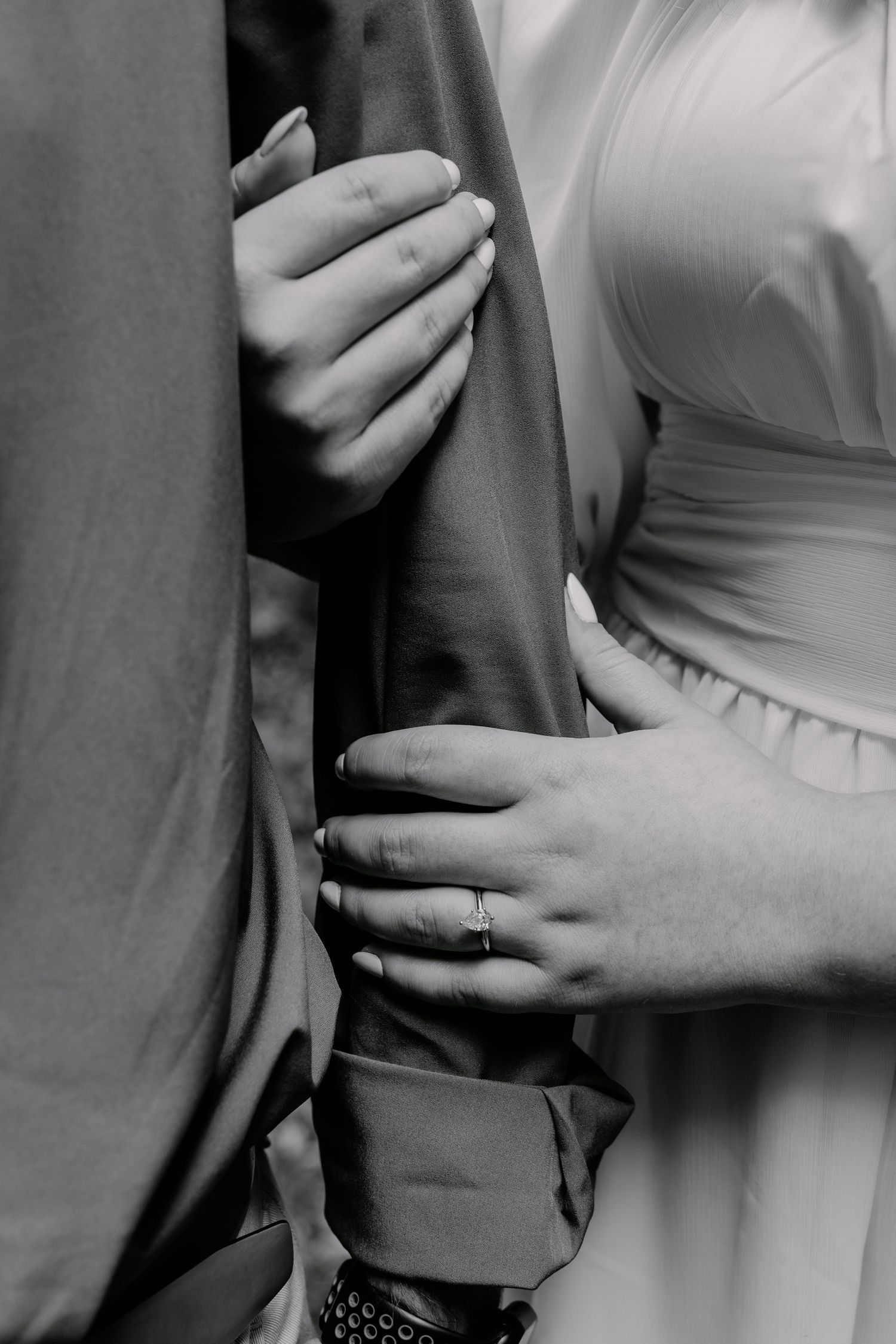 Close-up black and white photo of couple's hands showing engagement ring.