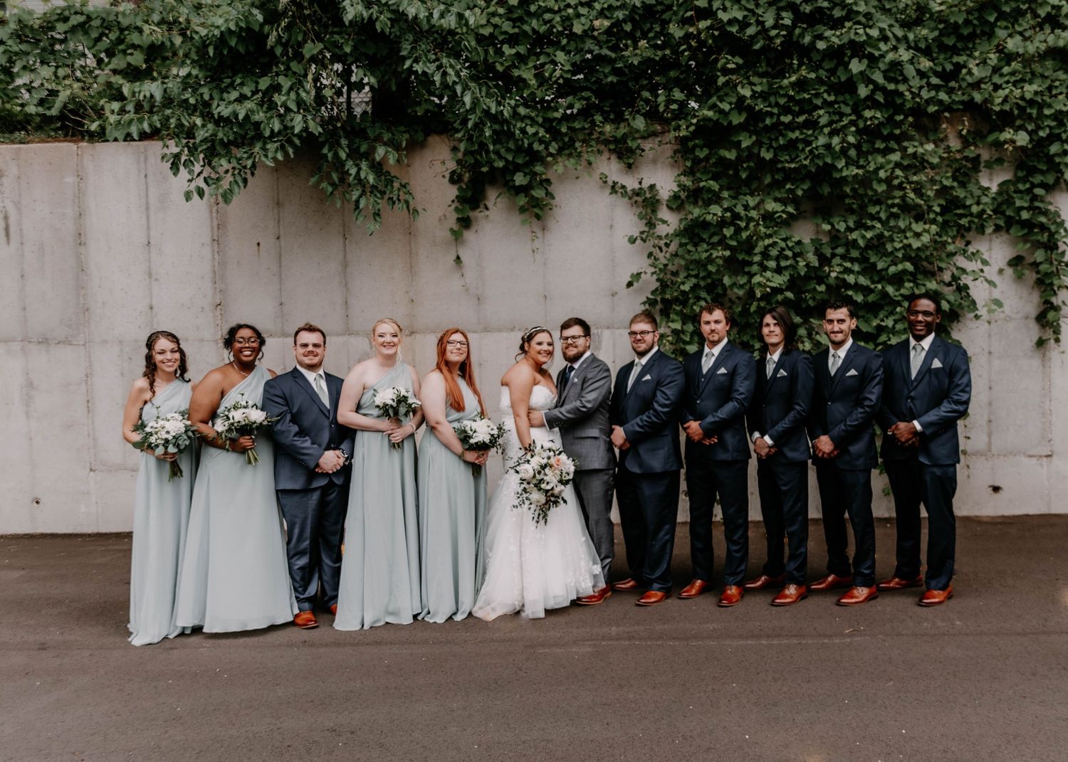 Wedding party lined up against an ivy-covered wall for formal portraits.