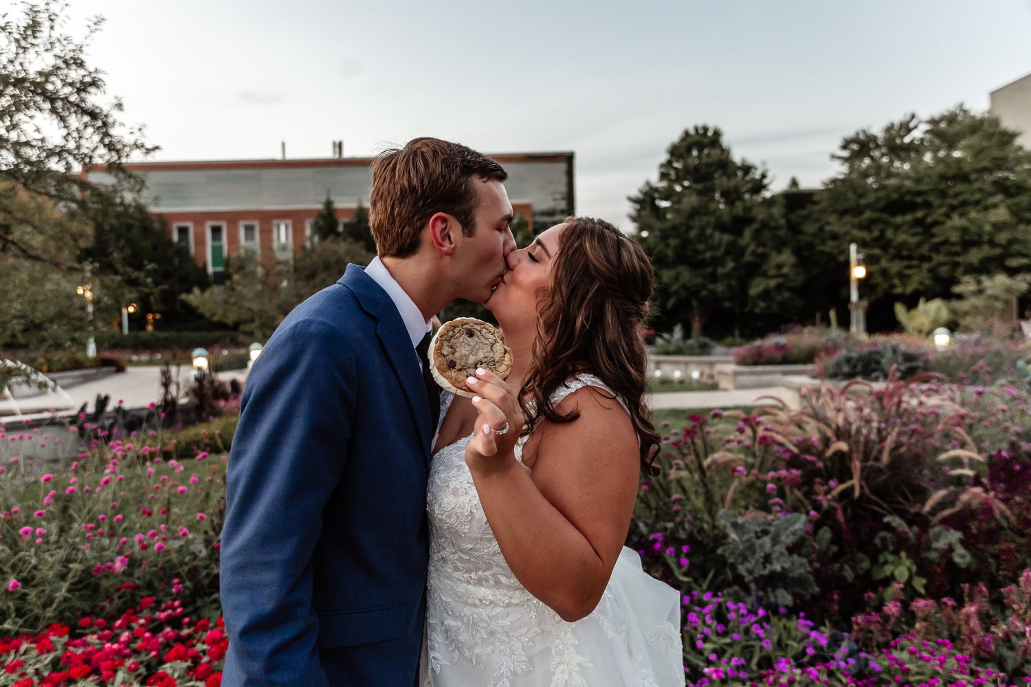 Bride and groom share a kiss in a blooming garden with colorful flowers.