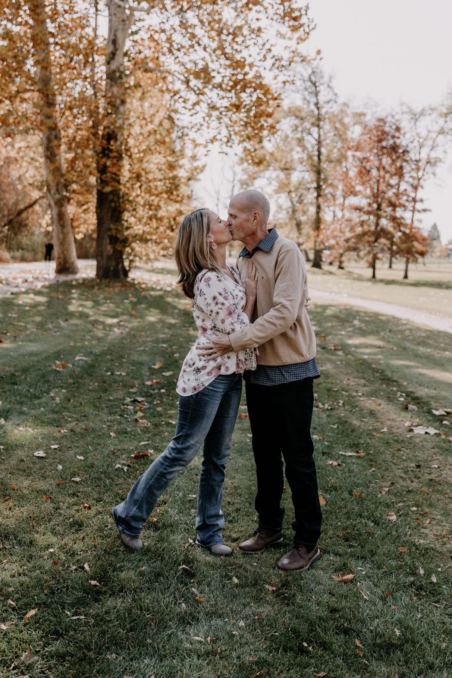 Romantic couple embracing on grassy lawn with autumn trees in background.