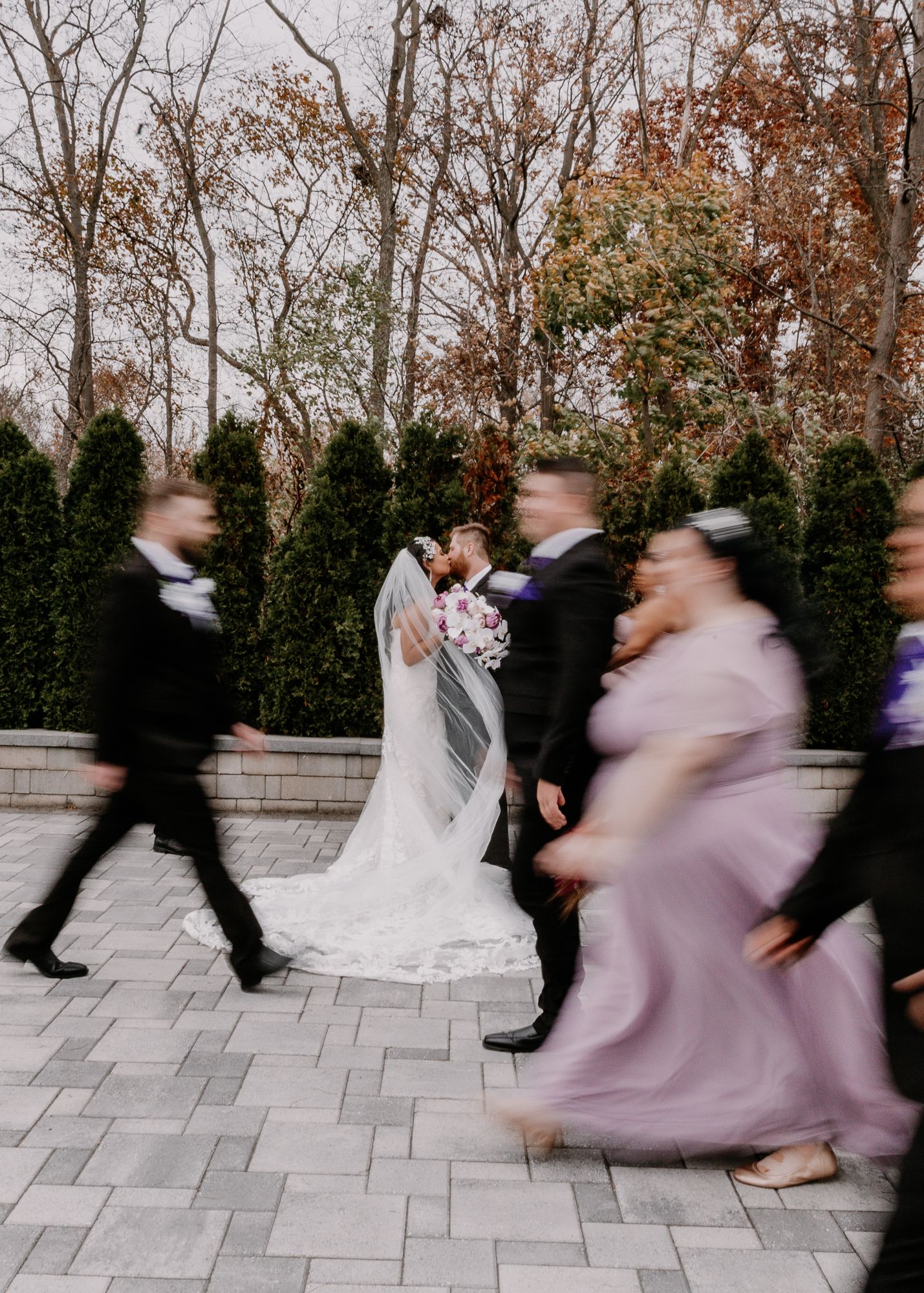 Wedding party members blur past as they walk by the bride and groom in an artistic motion shot.