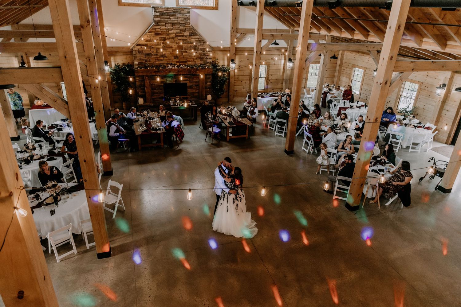 Overhead view of wedding reception in rustic barn venue with colorful dance floor lighting.