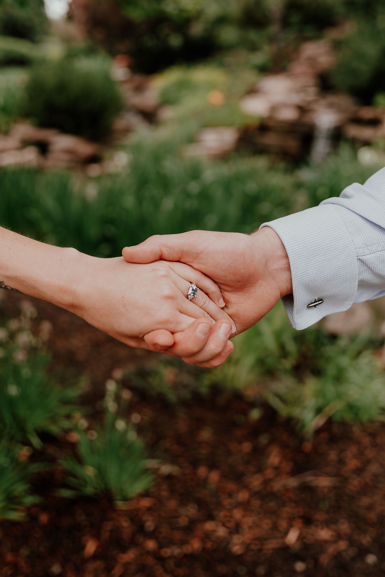 Romantic outdoor engagement photo showing couple holding hands with ring in focus.