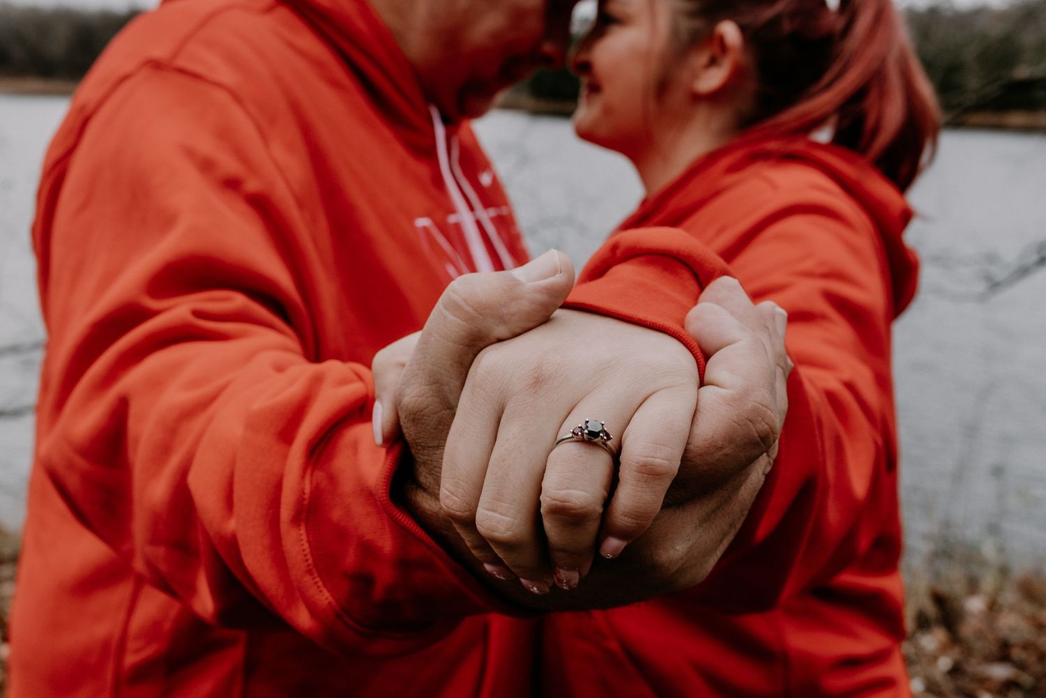 Two people wearing red hoodies hold hands to display their matching rings.
