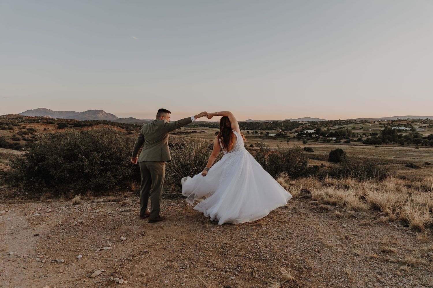Couple in wedding attire posing together on a desert ridge at sunset.