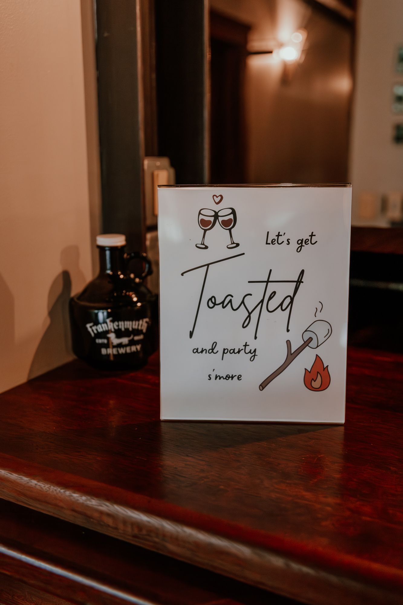 Wedding reception sign reading 'Let's get toasted and party' next to a whiskey bottle.