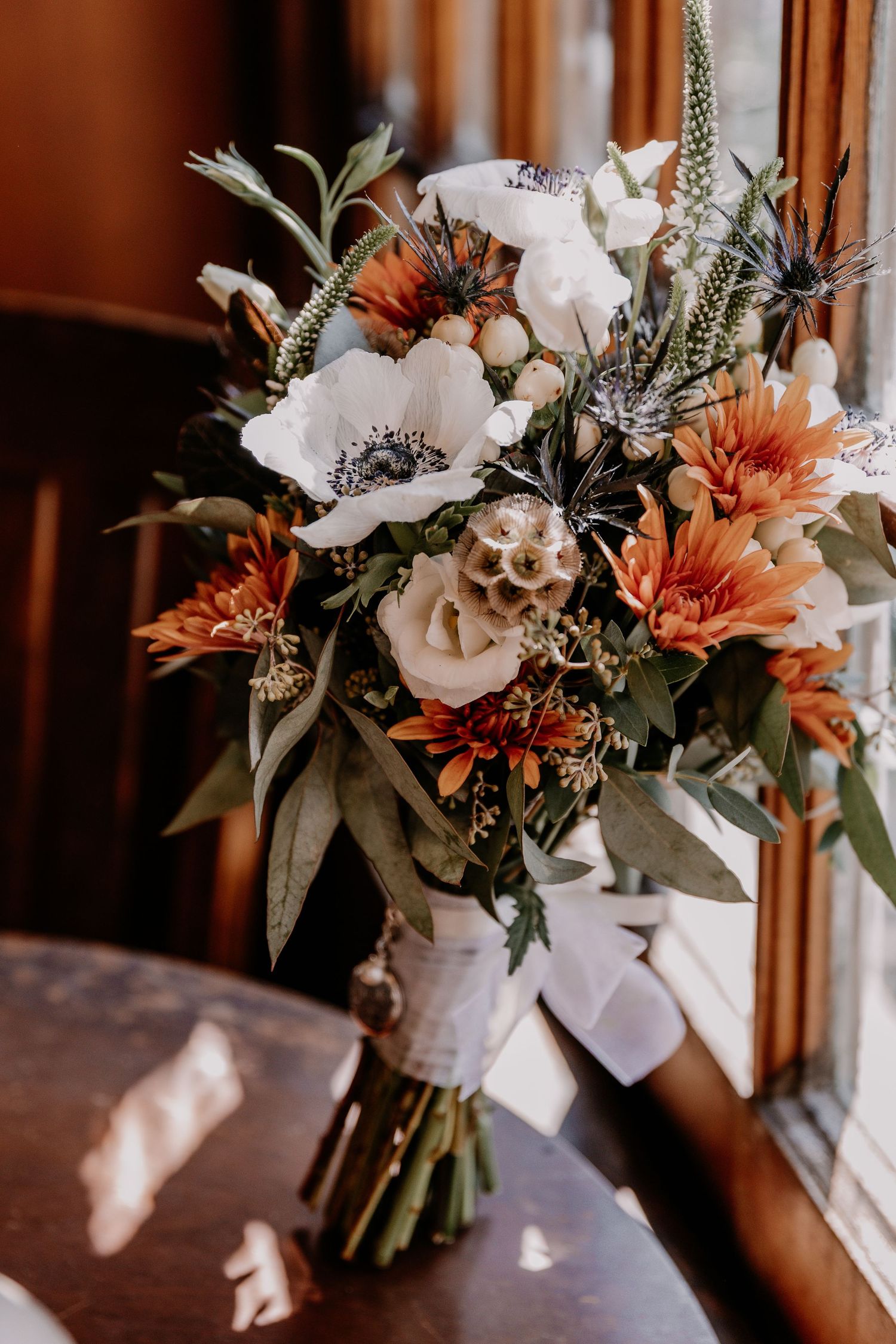 Beautiful wedding bouquet with orange and white flowers and green foliage arranged naturally in warm lighting.