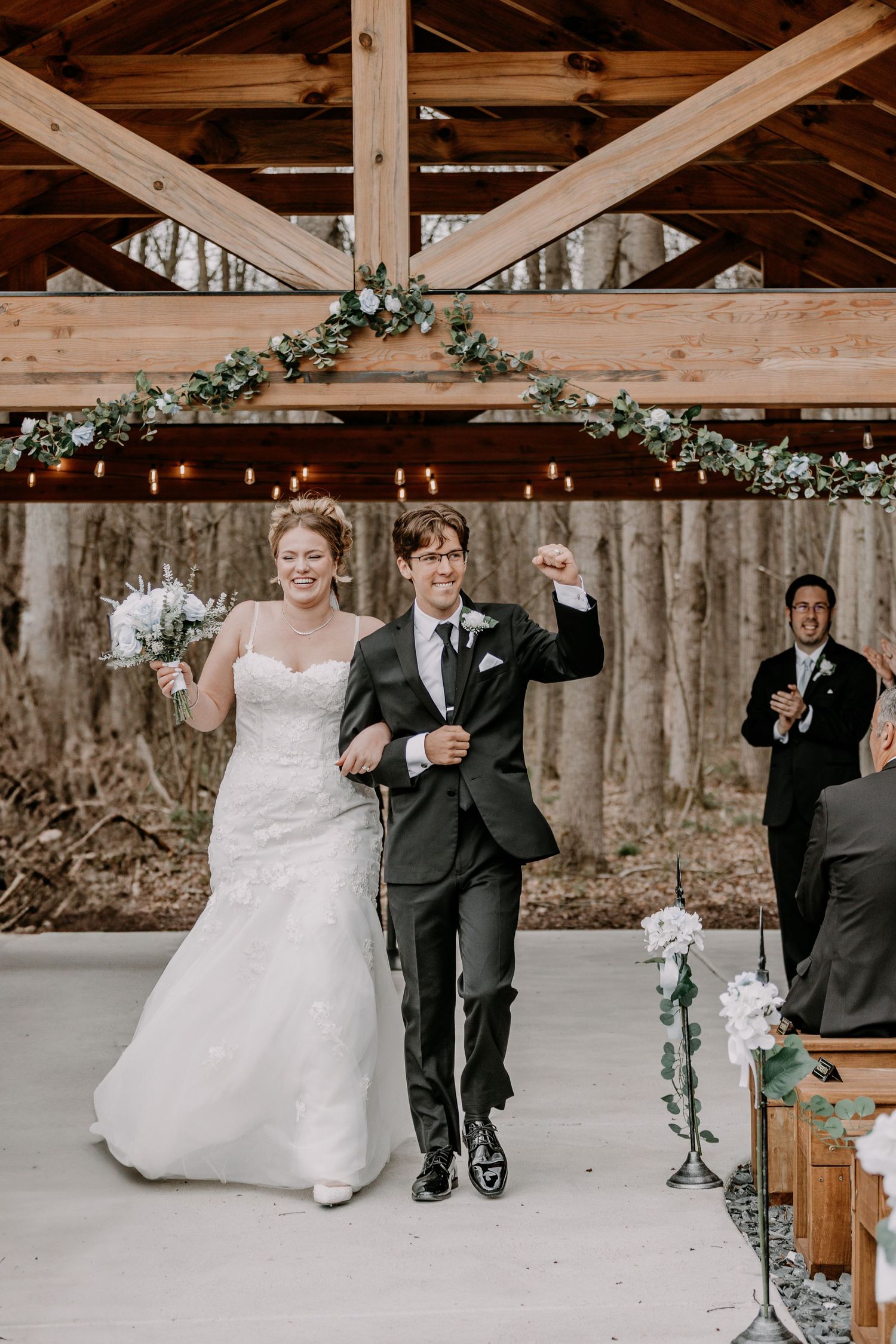 A series of wooden benches decorated with greenery inside a rustic barn venue.