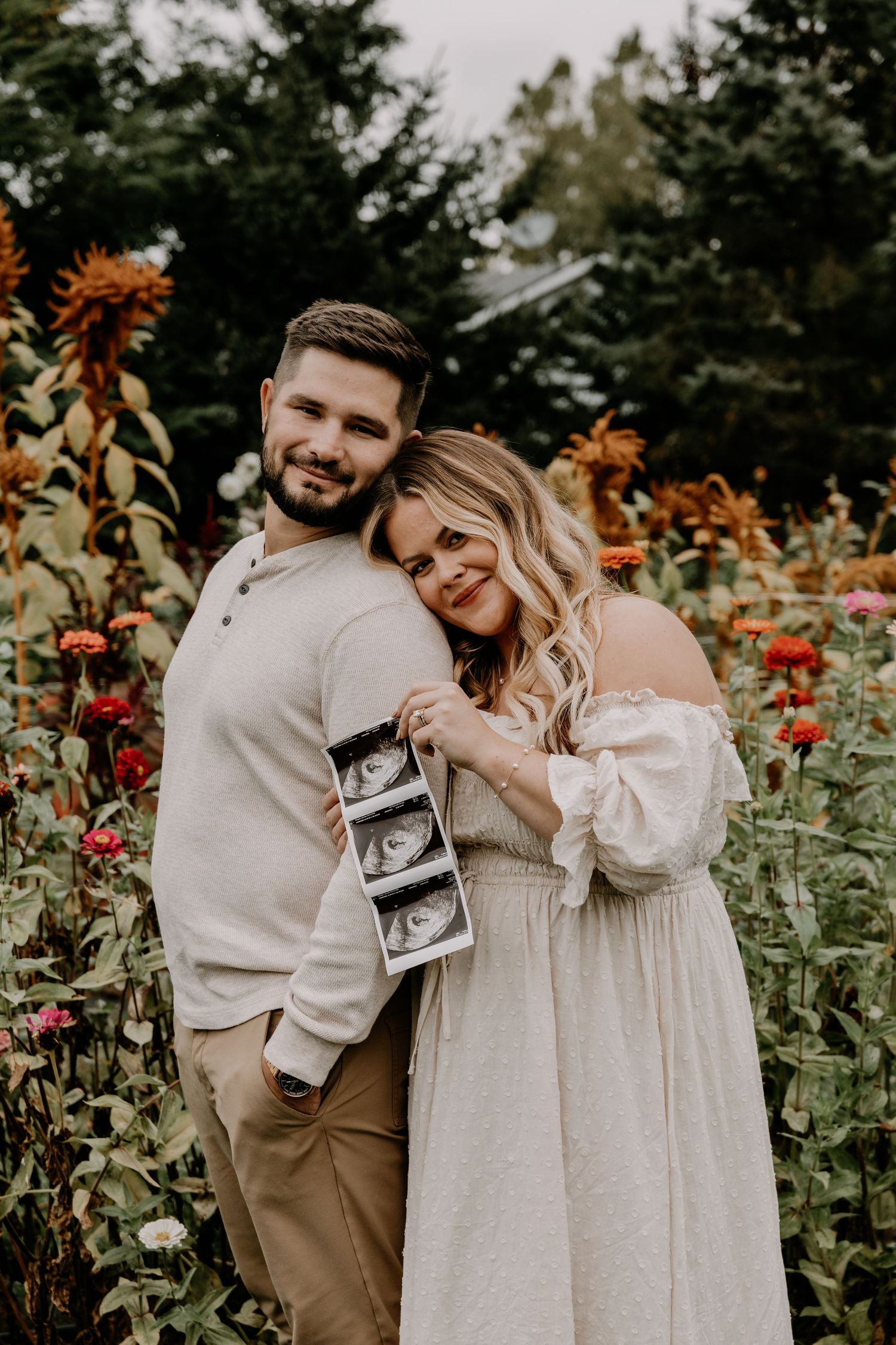 Emotional garden photoshoot with couple holding ultrasound photos among flowers.