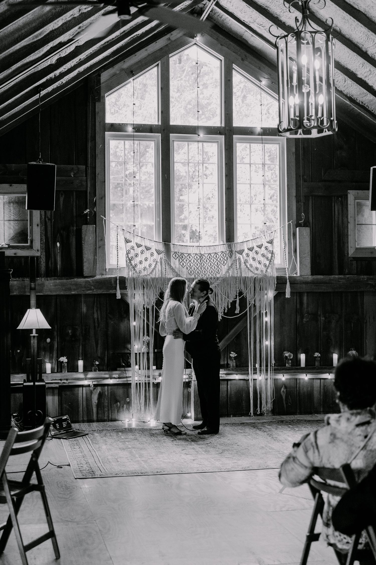 Wedding ceremony in rustic wooden venue with large windows and macrame backdrop.