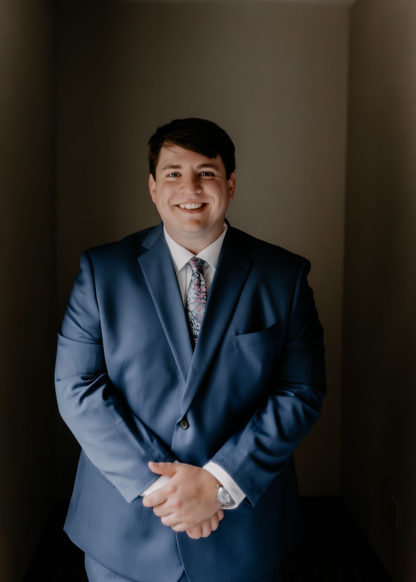 Person in navy blue suit smiling in indoor portrait setting.