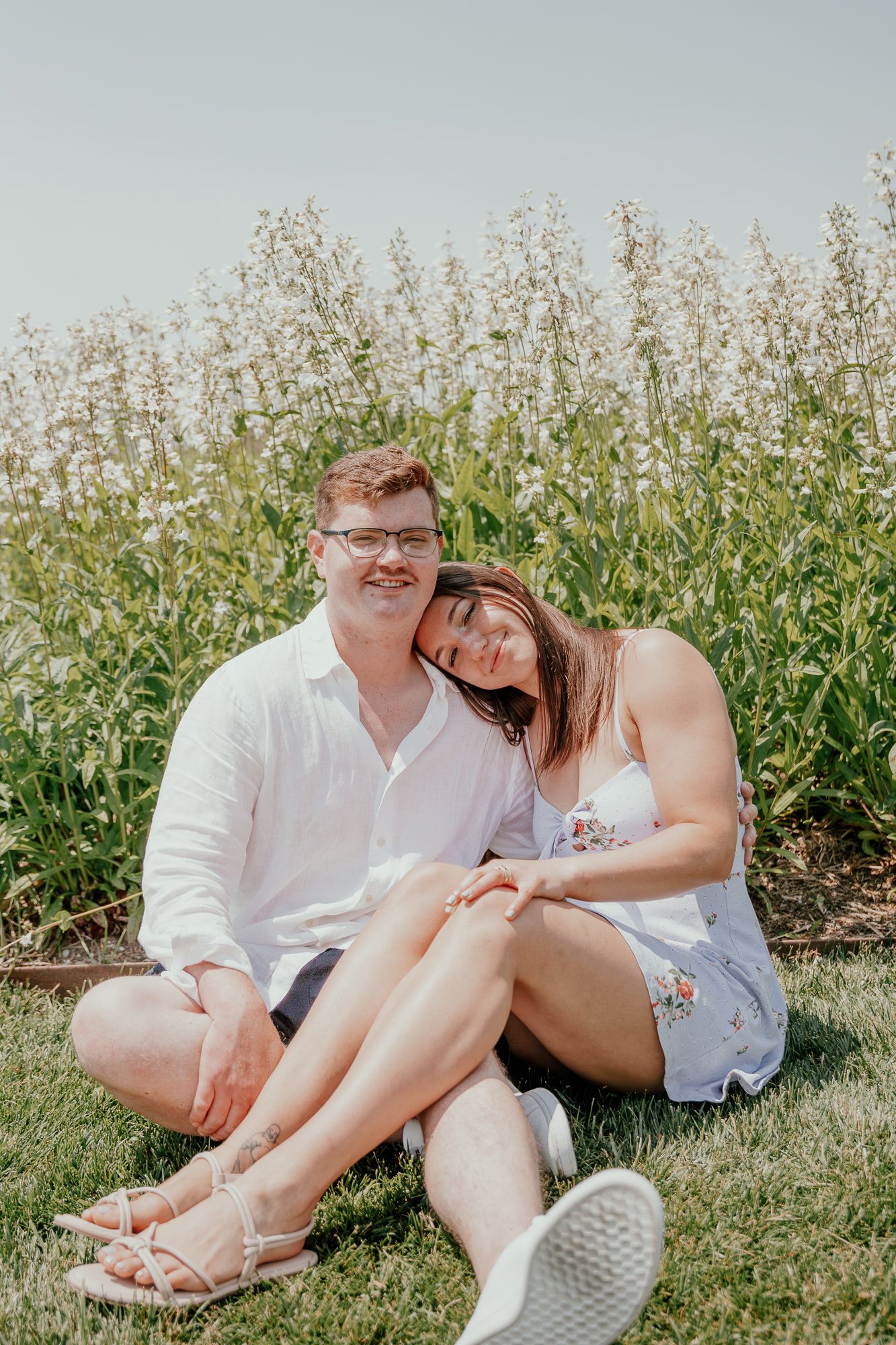 A couple relaxes on grass near blooming wildflowers on a sunny summer day.