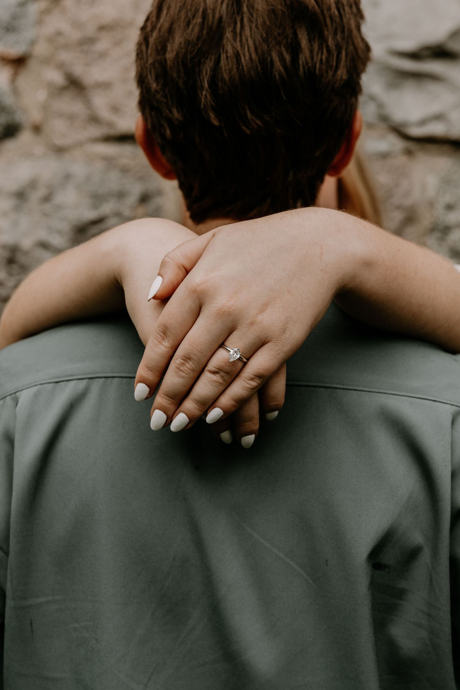 Close-up of hands with engagement ring wrapped around shoulders in an embrace.