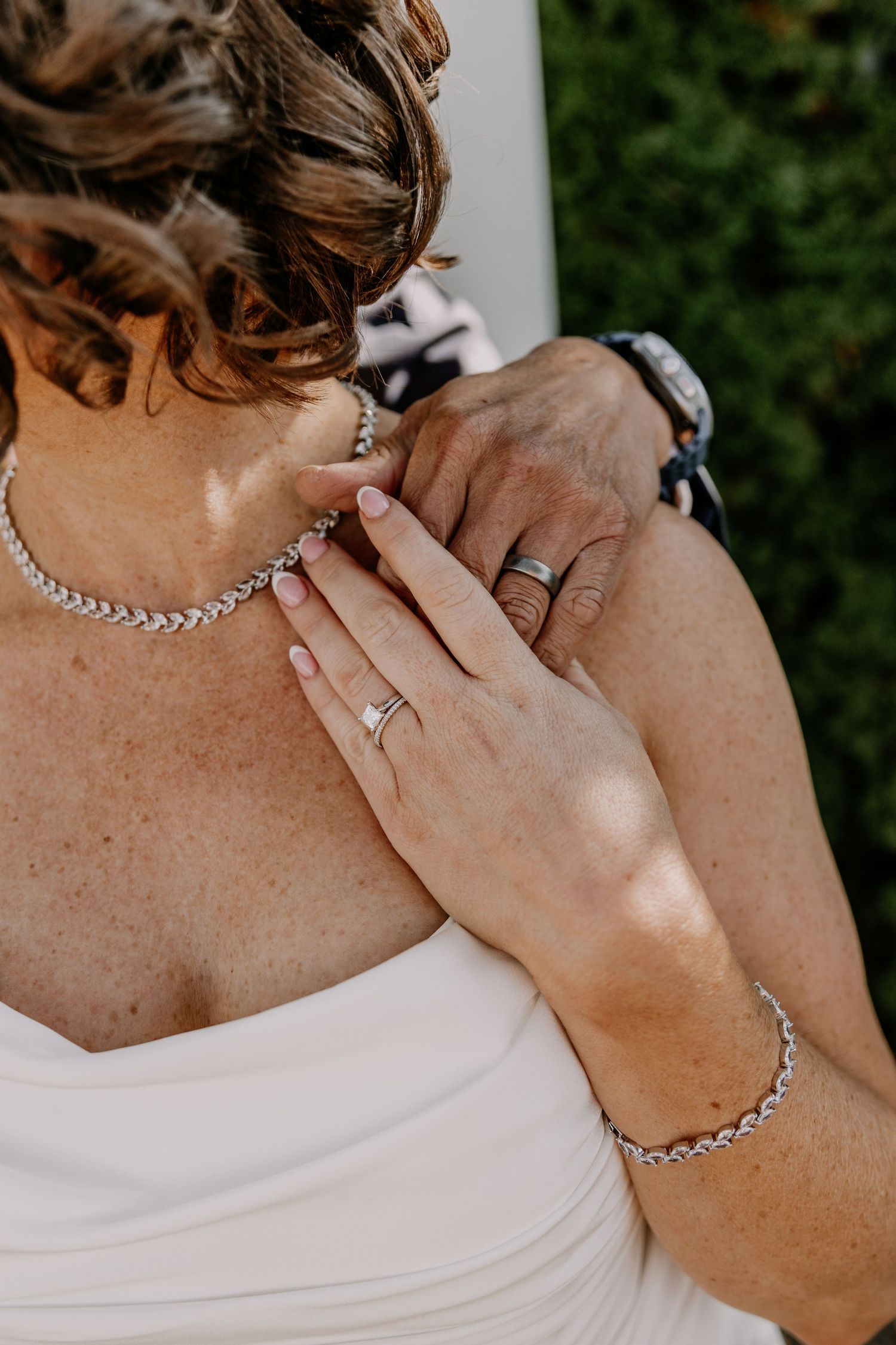 Close-up detail shots of bridal jewelry including a diamond ring and silver chain necklace against white dress.