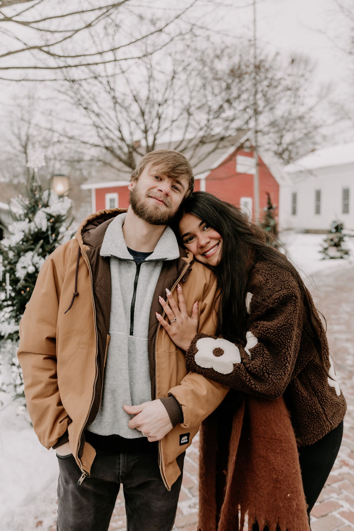 A cozy winter portrait against a snowy landscape with red and white buildings visible in the distance.