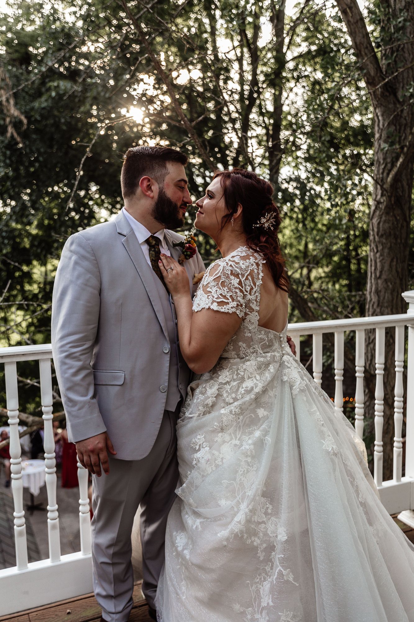 Romantic wedding portraits on a white railing deck surrounded by trees at golden hour.