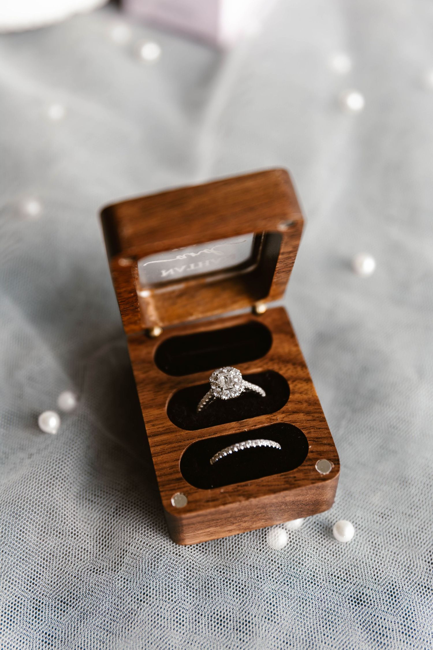 Diamond engagement ring and wedding bands displayed in wooden ring box.