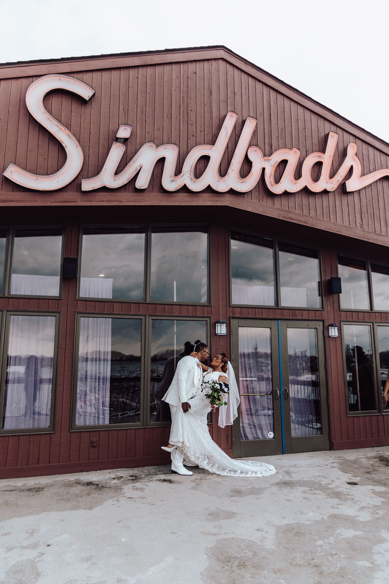 Wedding couple poses outside Sindbads restaurant in elegant white attire.