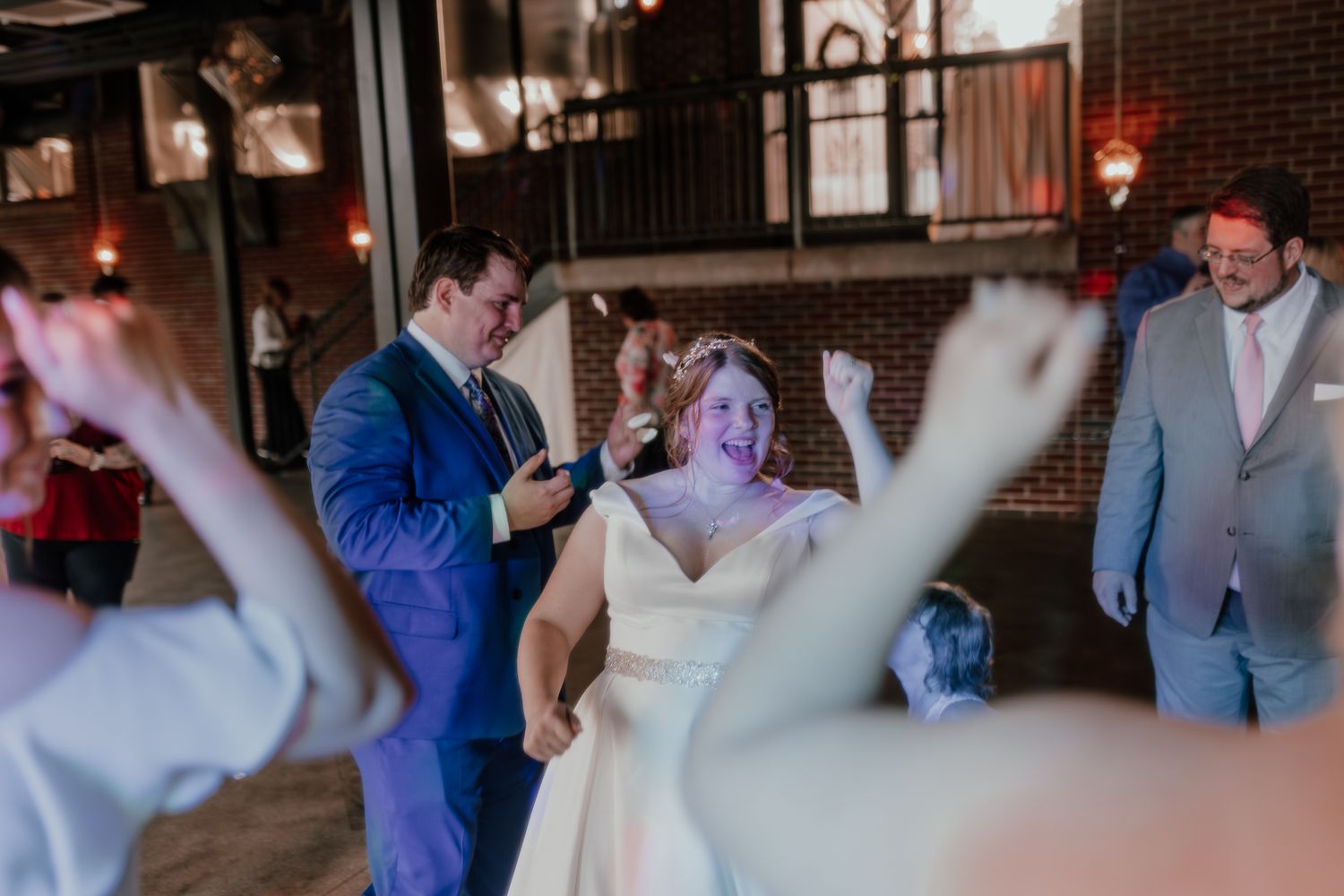 Wedding couple dancing and celebrating with guests at an indoor reception venue.