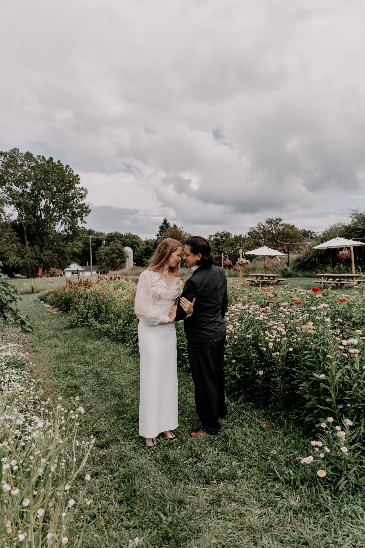 Couple sharing an intimate moment in a blooming wildflower meadow with cloudy skies overhead.