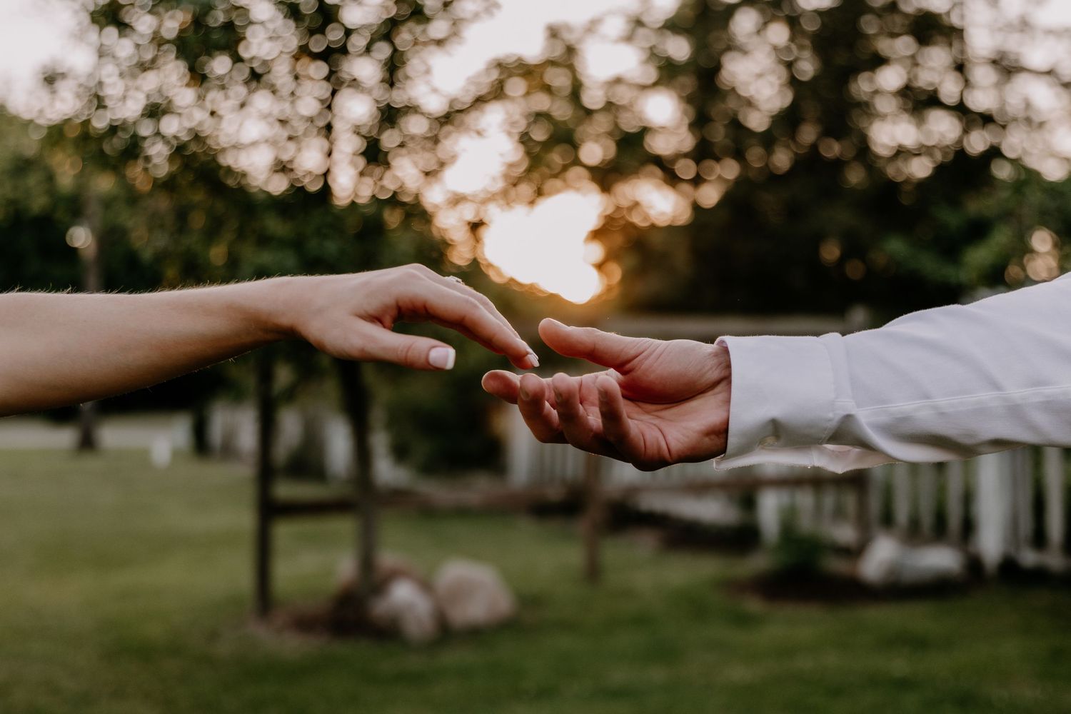 Two people gently touching fingertips at sunset in a lush green garden, symbolizing love and connection.