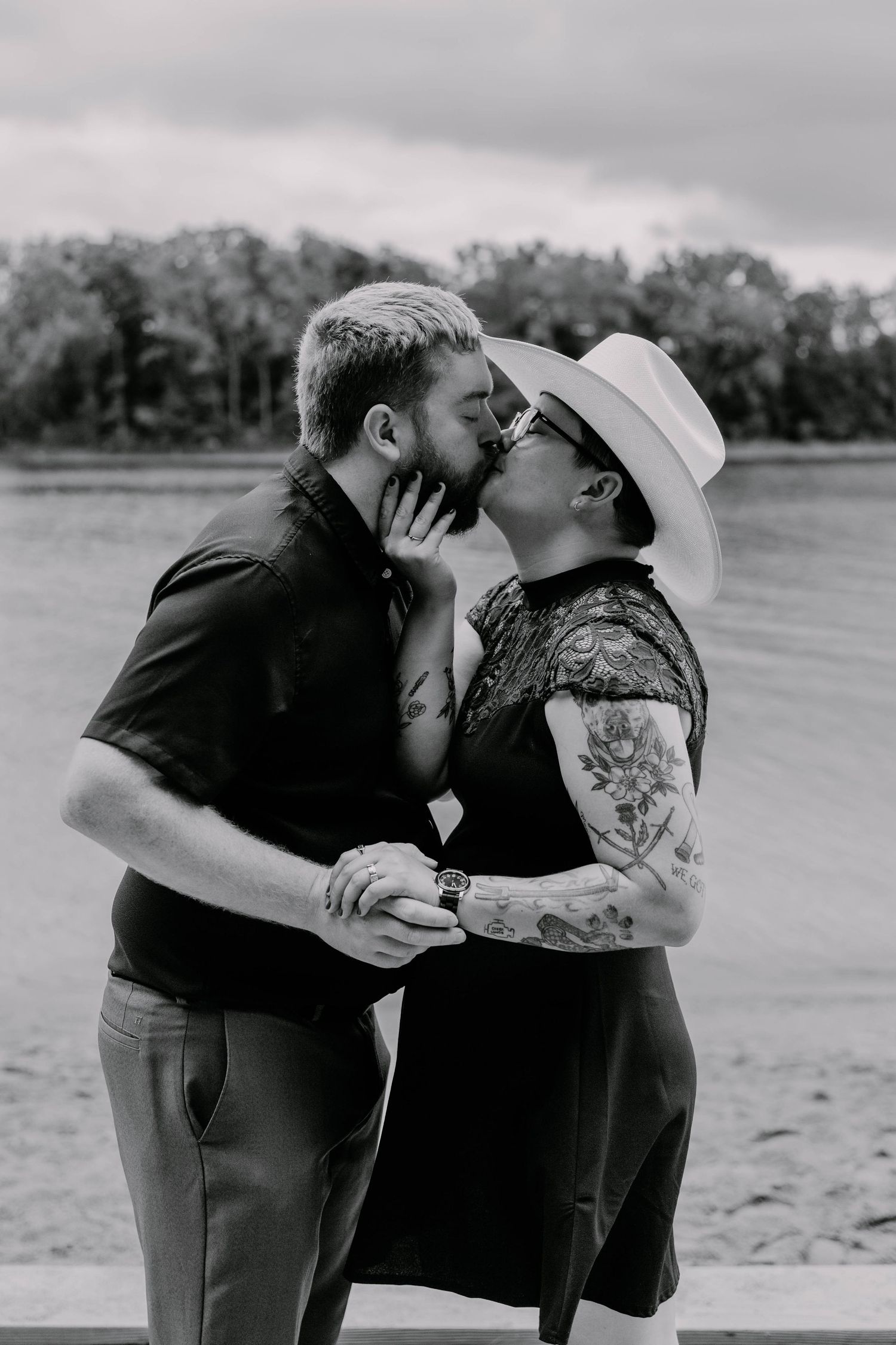 Romantic couple sharing an intimate moment by a lake with trees in the background.
