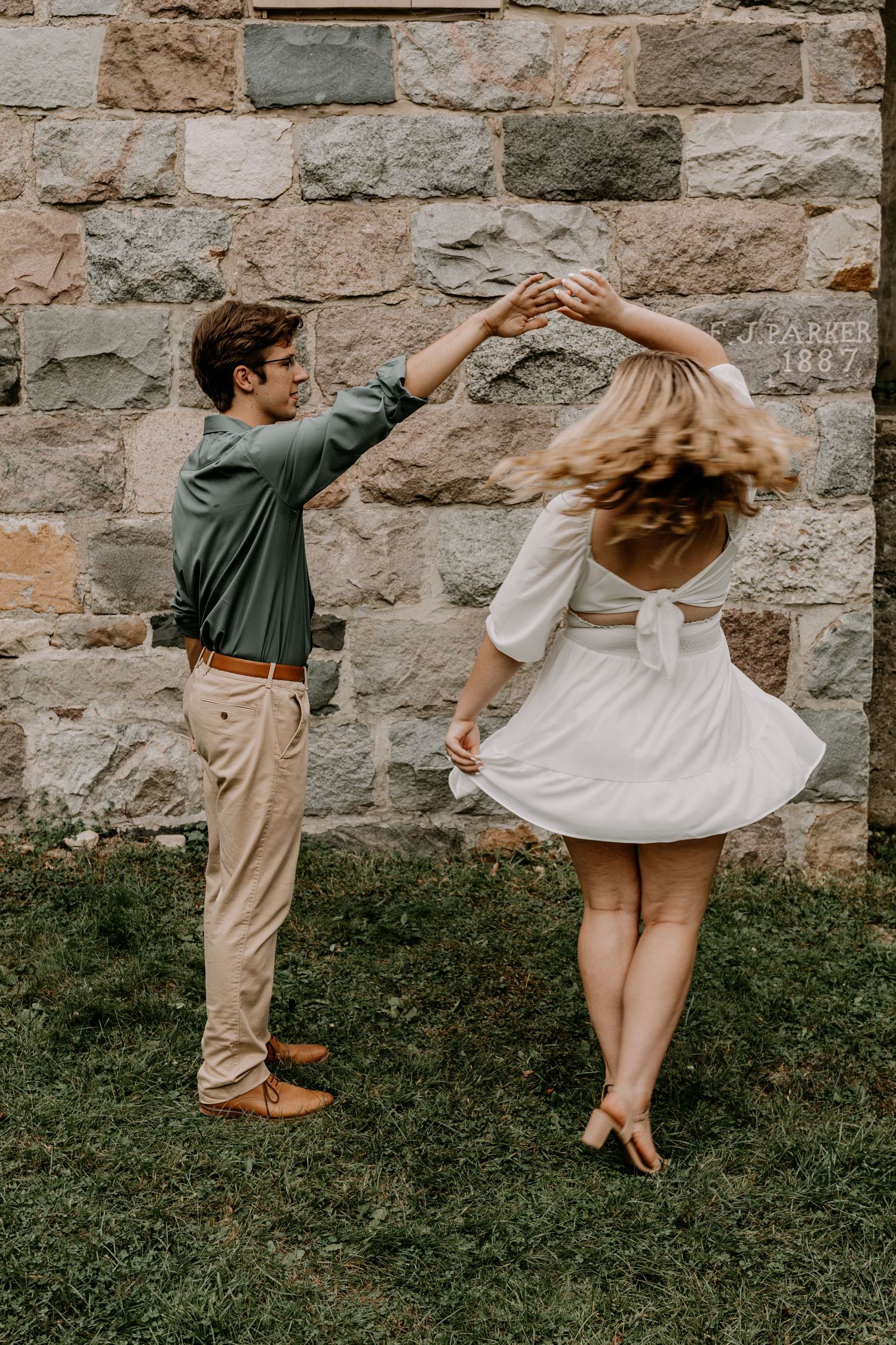 Couple dancing against stone wall backdrop during romantic outdoor photoshoot.