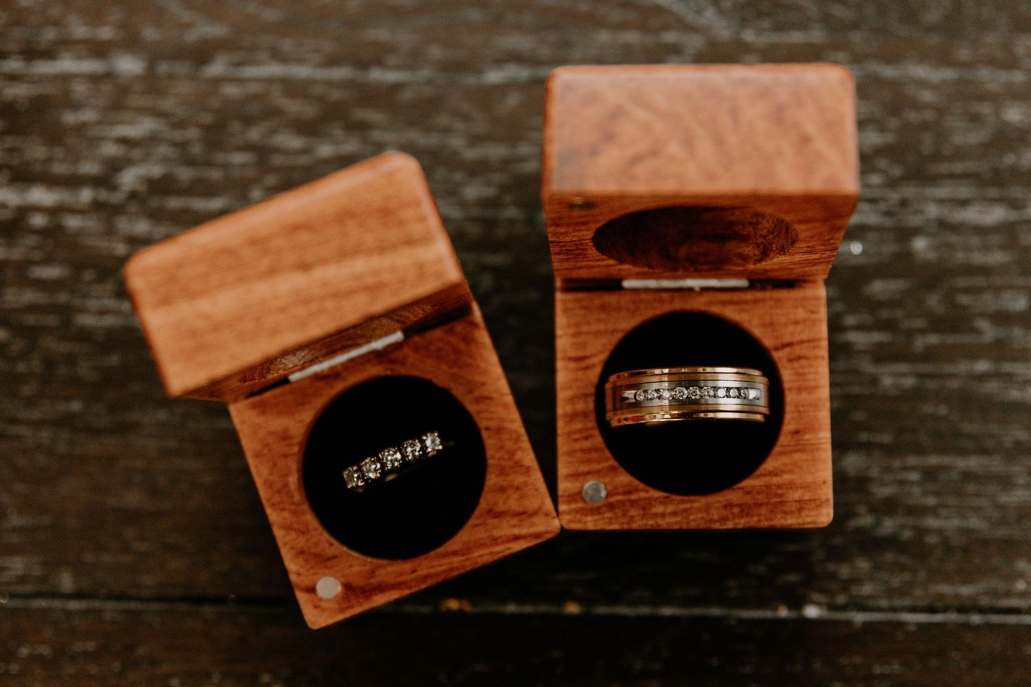 Two wooden ring boxes containing wedding bands on a rustic wooden surface.