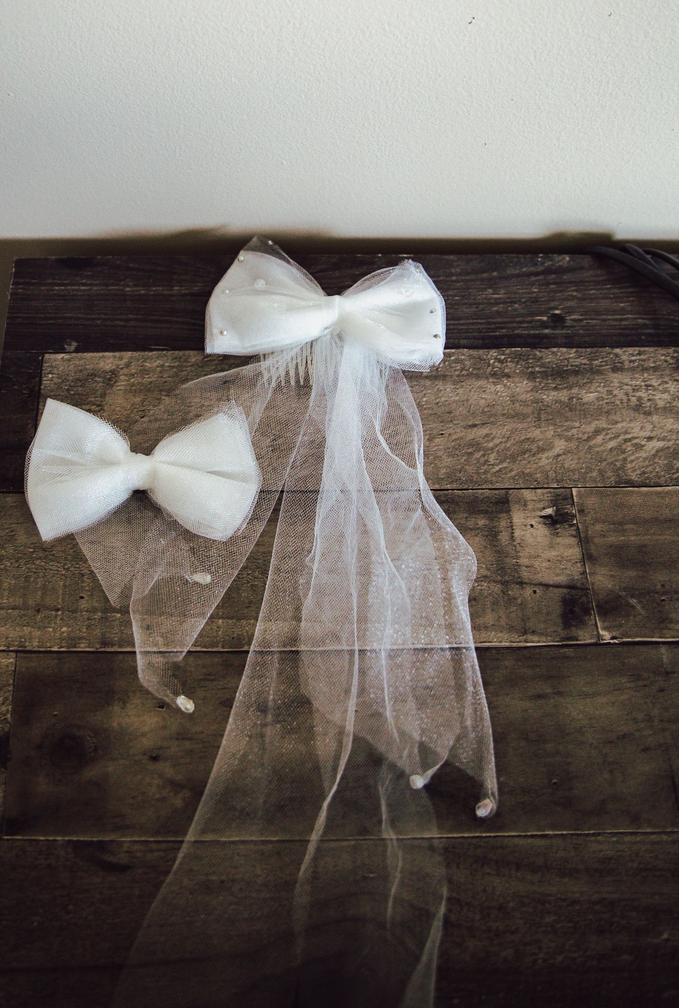 Two white tulle wedding bows displayed on rustic wooden boards.