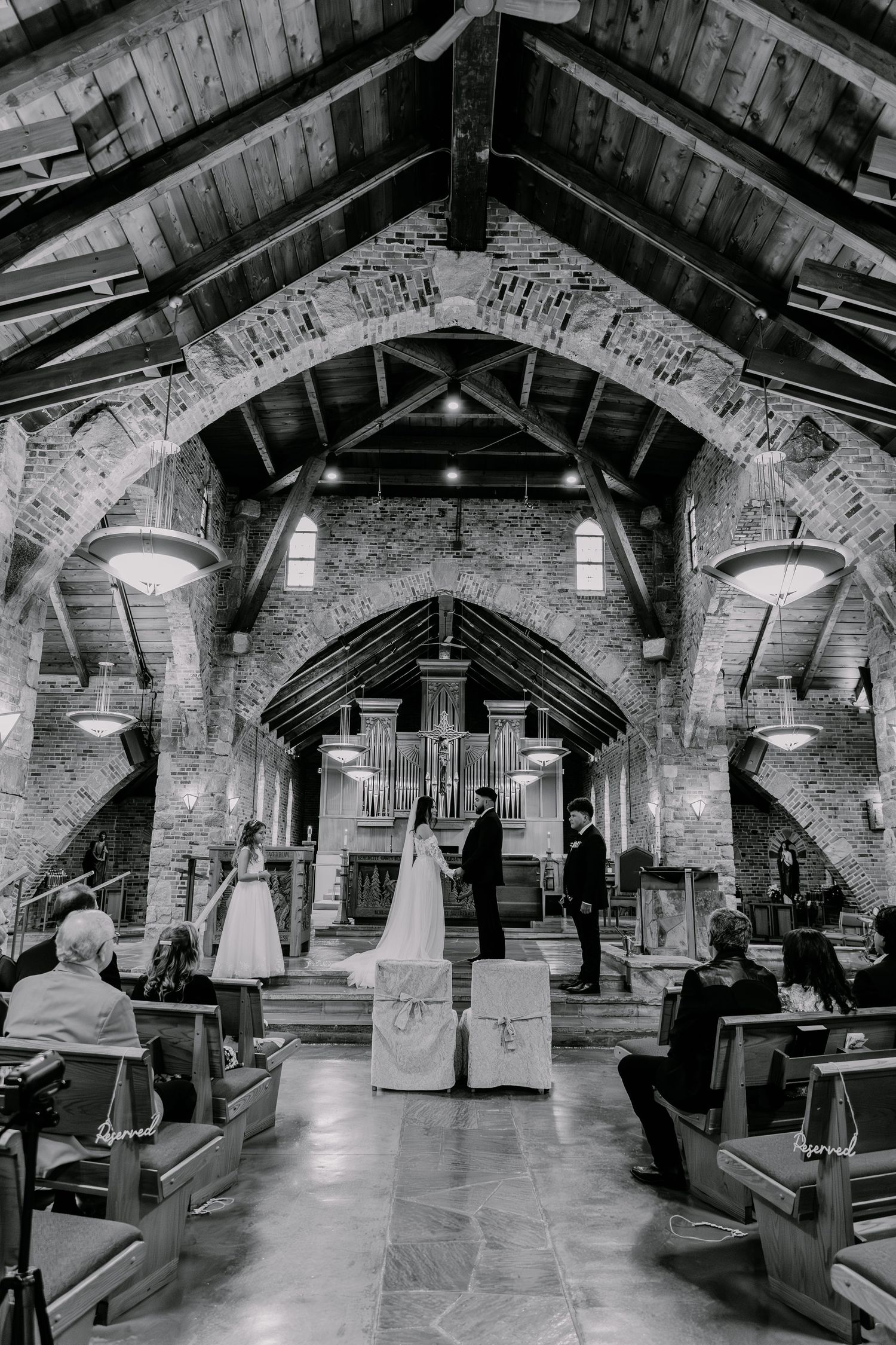 Black and white photo of a church wedding ceremony in a gothic stone chapel with wooden beams and dramatic arches.