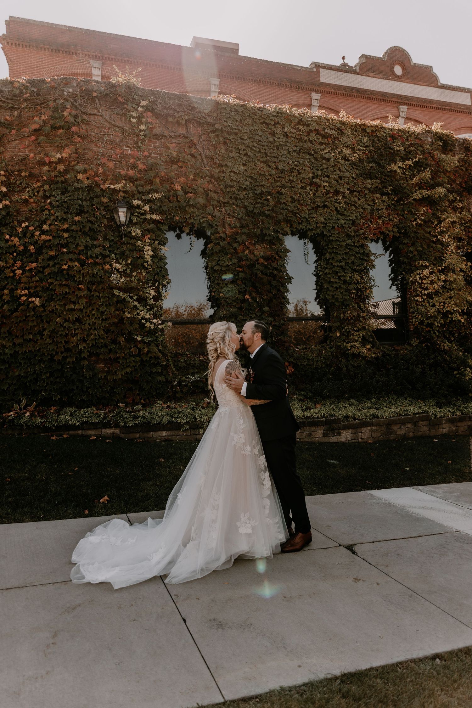 A couple shares a romantic moment against an ivy-covered wall during their wedding photoshoot.