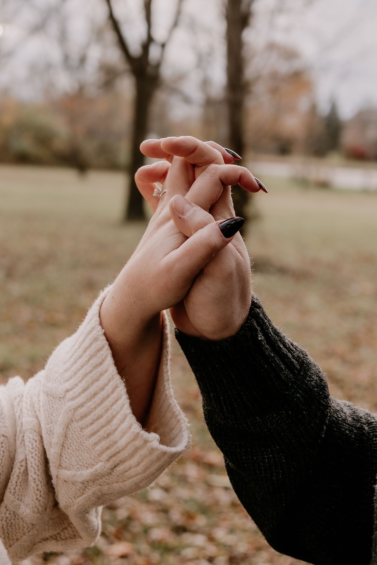 Two people holding hands in white and black sweaters against an autumn outdoor background.