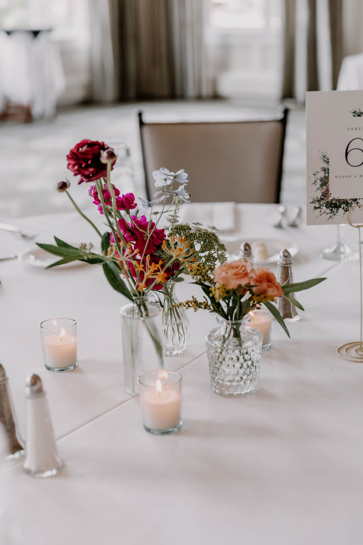 Wedding reception table setting with delicate floral arrangements in crystal vases and glowing candles.