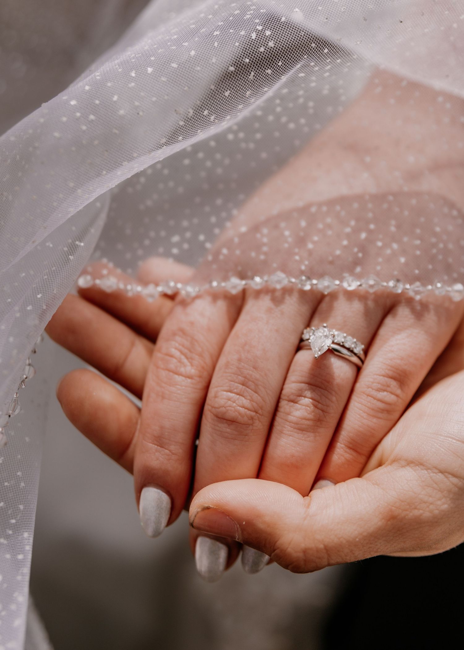 Detailed shot of wedding rings and hands through delicate veil material.